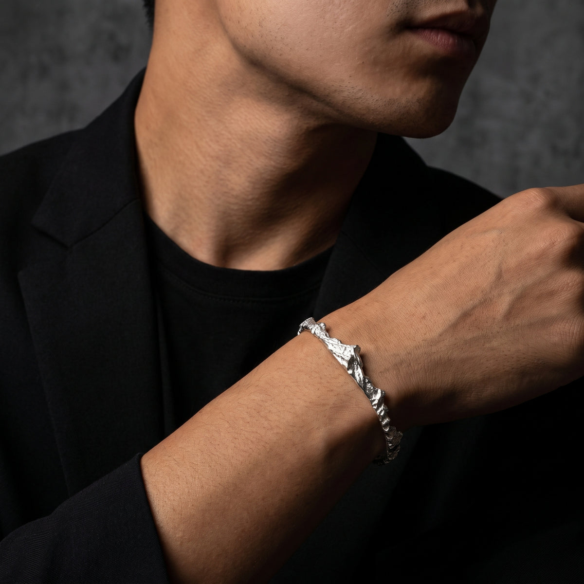 Angled view of a model wearing the textured silver mountain ridge cuff bracelet with a black blazer.