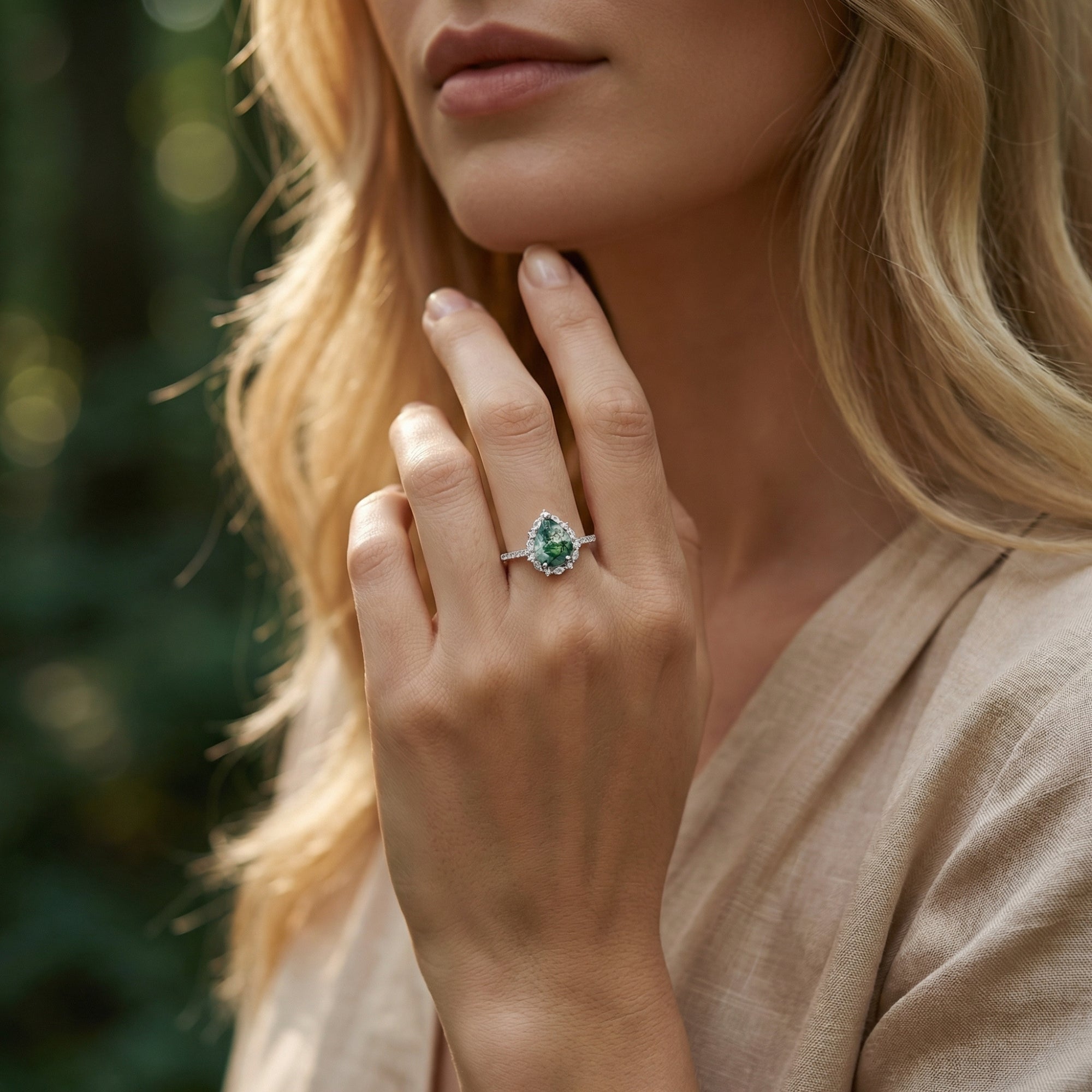 Sterling silver moss agate ring with a pear cut center stone and diamond halo, worn by a model in natural light.