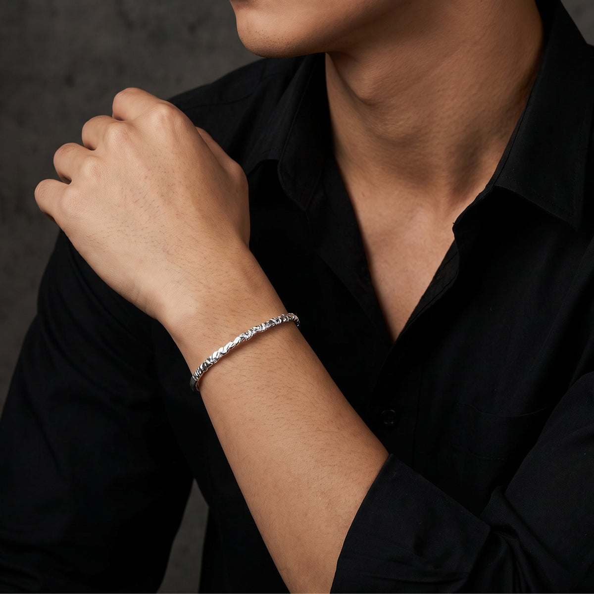Man in a black shirt wearing the carved silver ridge cuff bracelet with his hand raised near his shoulder.