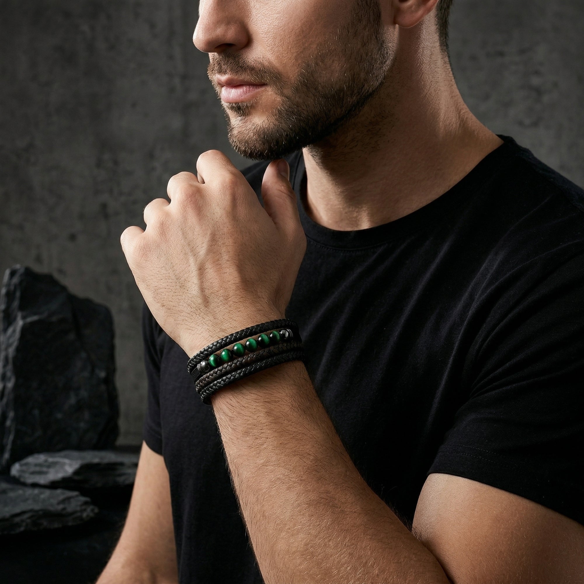 Men's black braided leather bracelet with green tiger eye beads styled on a model's wrist.