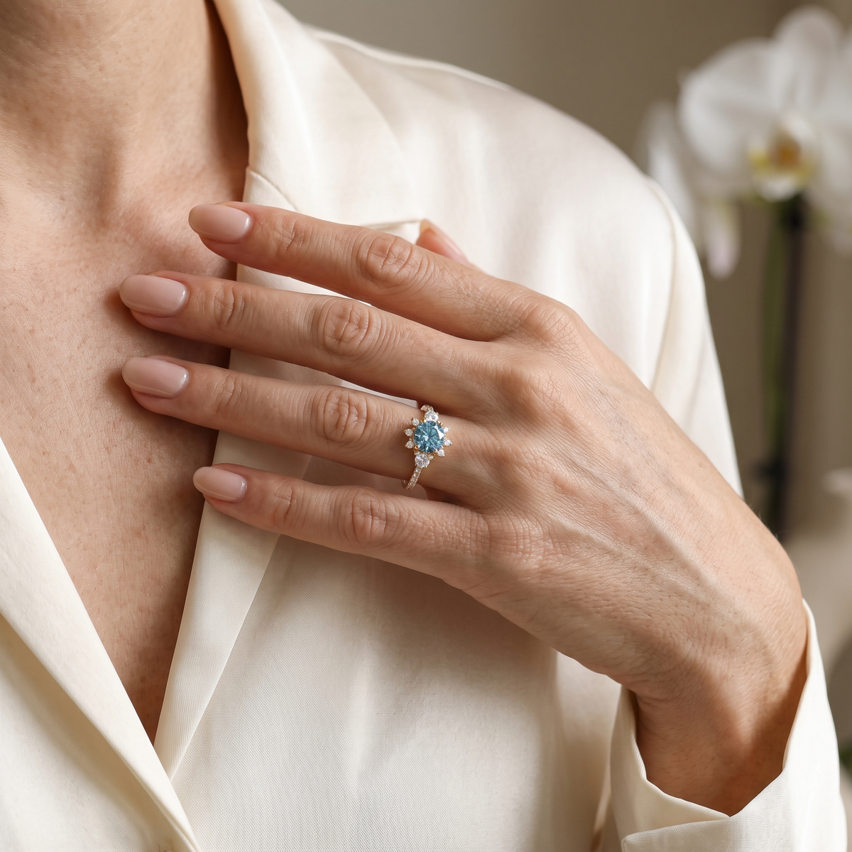 Model displaying a rose gold teal blue moissanite engagement ring against a silk blouse.