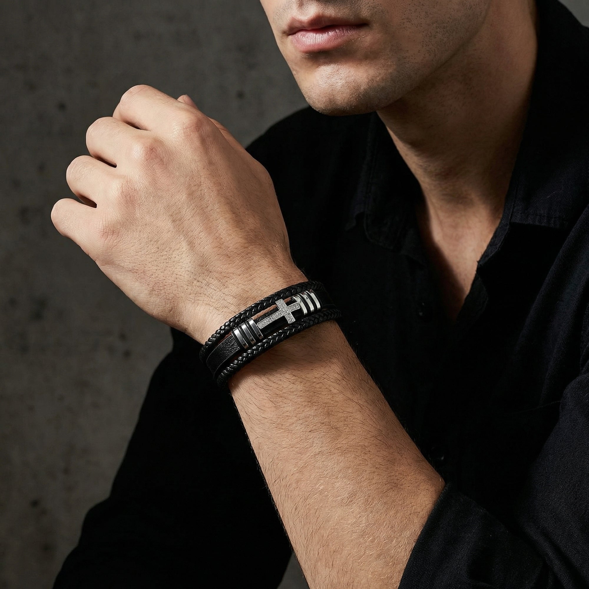 Aegis Cross Bracelet with stainless steel cross and black leather band worn by a man in a black shirt.