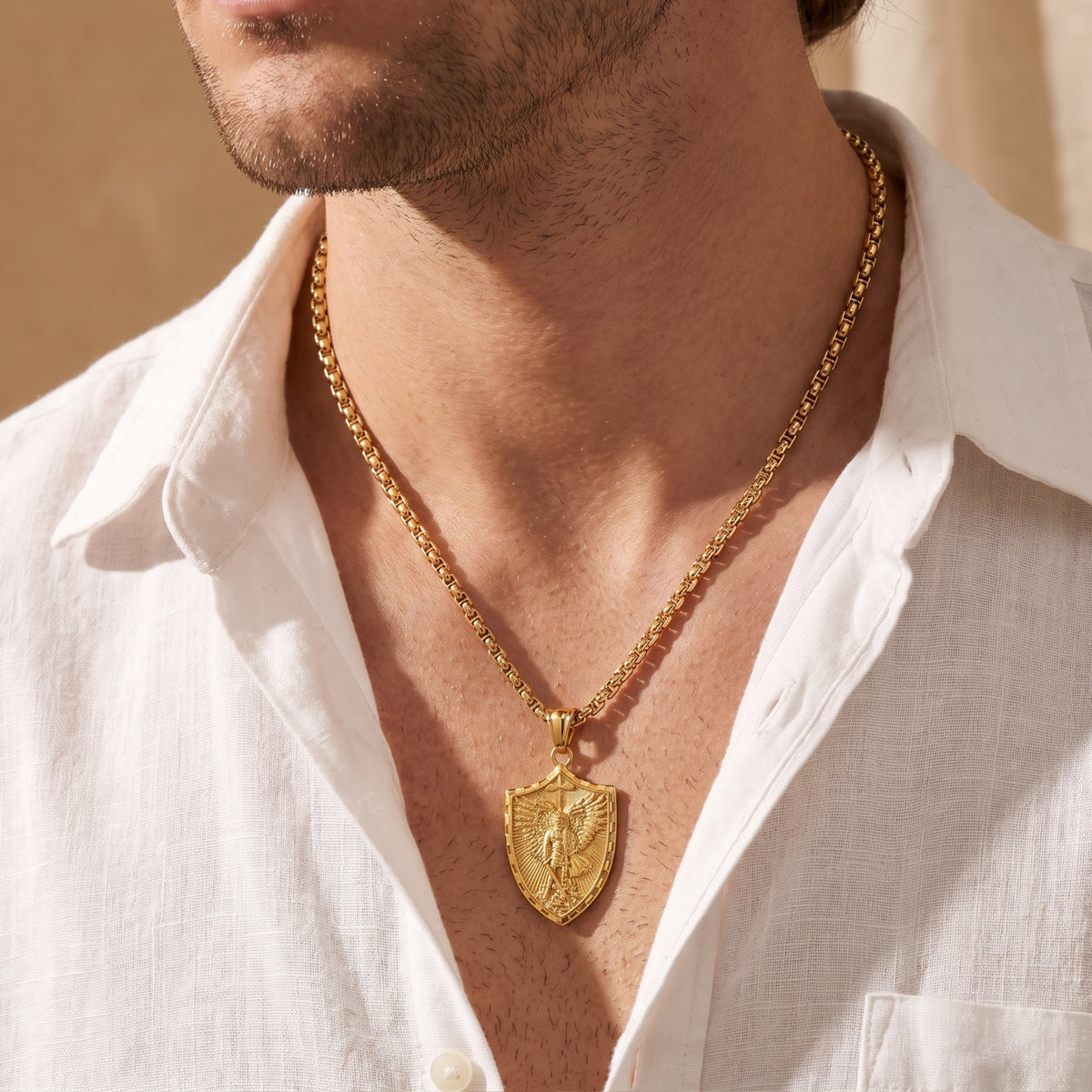 Front view of a man wearing the gold-tone archangel shield pendant over an unbuttoned white textured shirt.