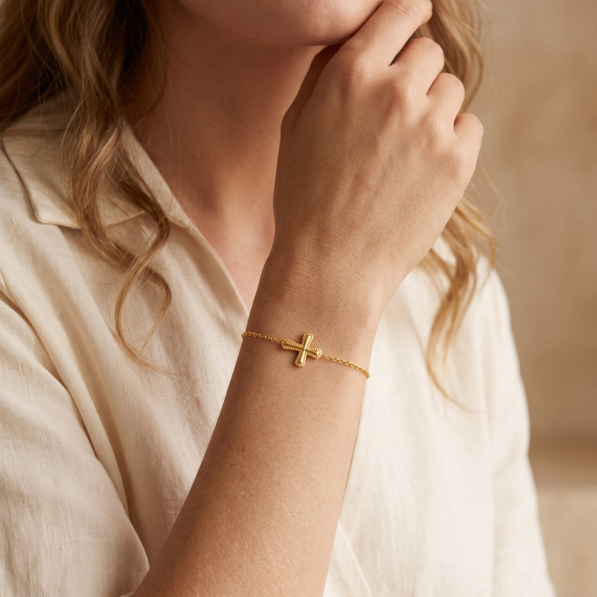Woman touching her chin while wearing a gold-toned cross bracelet on her wrist.