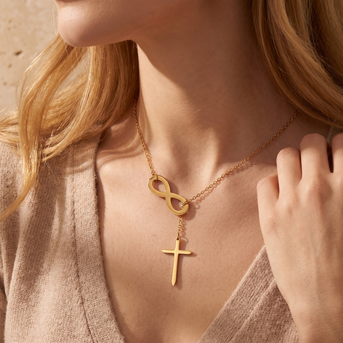 Gold-tone infinity and cross lariat necklace worn with a beige knit sweater