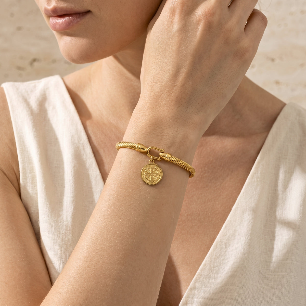 Close-up of a model wearing the gold-tone twisted cable medal bracelet on her wrist with a white sleeveless top.