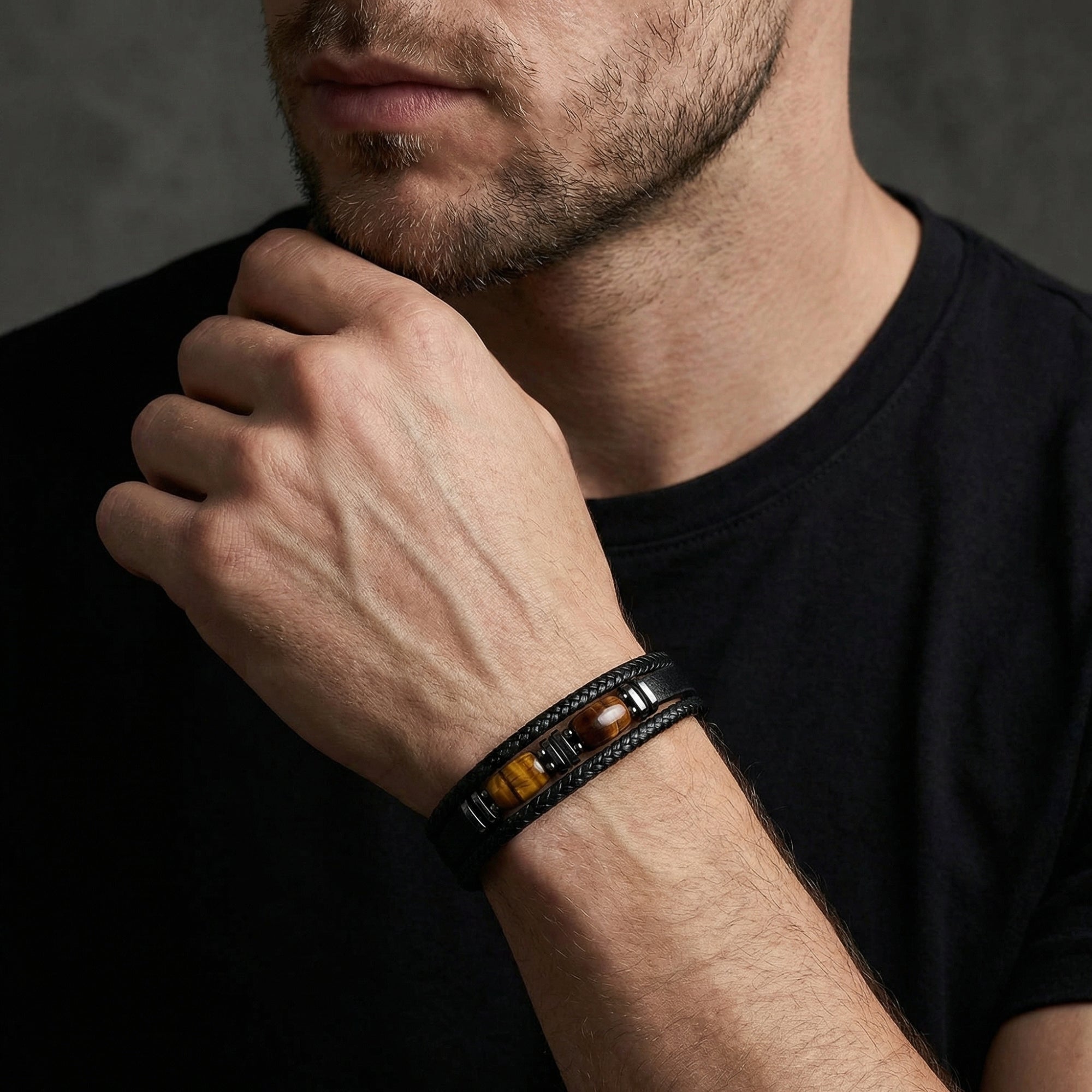 The Fortitude black braided leather and steel bracelet with tiger's eye barrel accents worn on a man's wrist.