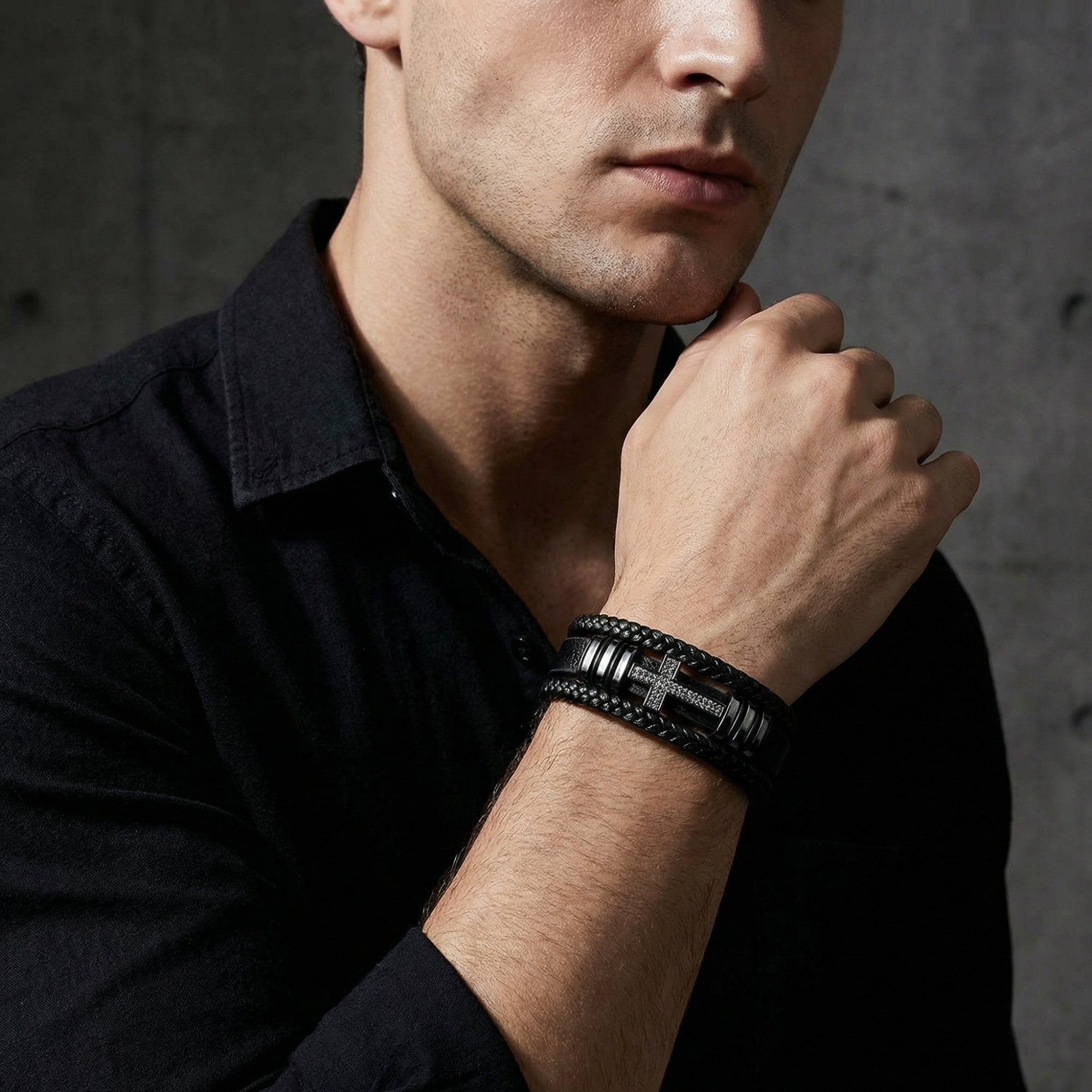 Men's black braided leather bracelet with a black PVD steel cross centerpiece shown on a model's wrist.