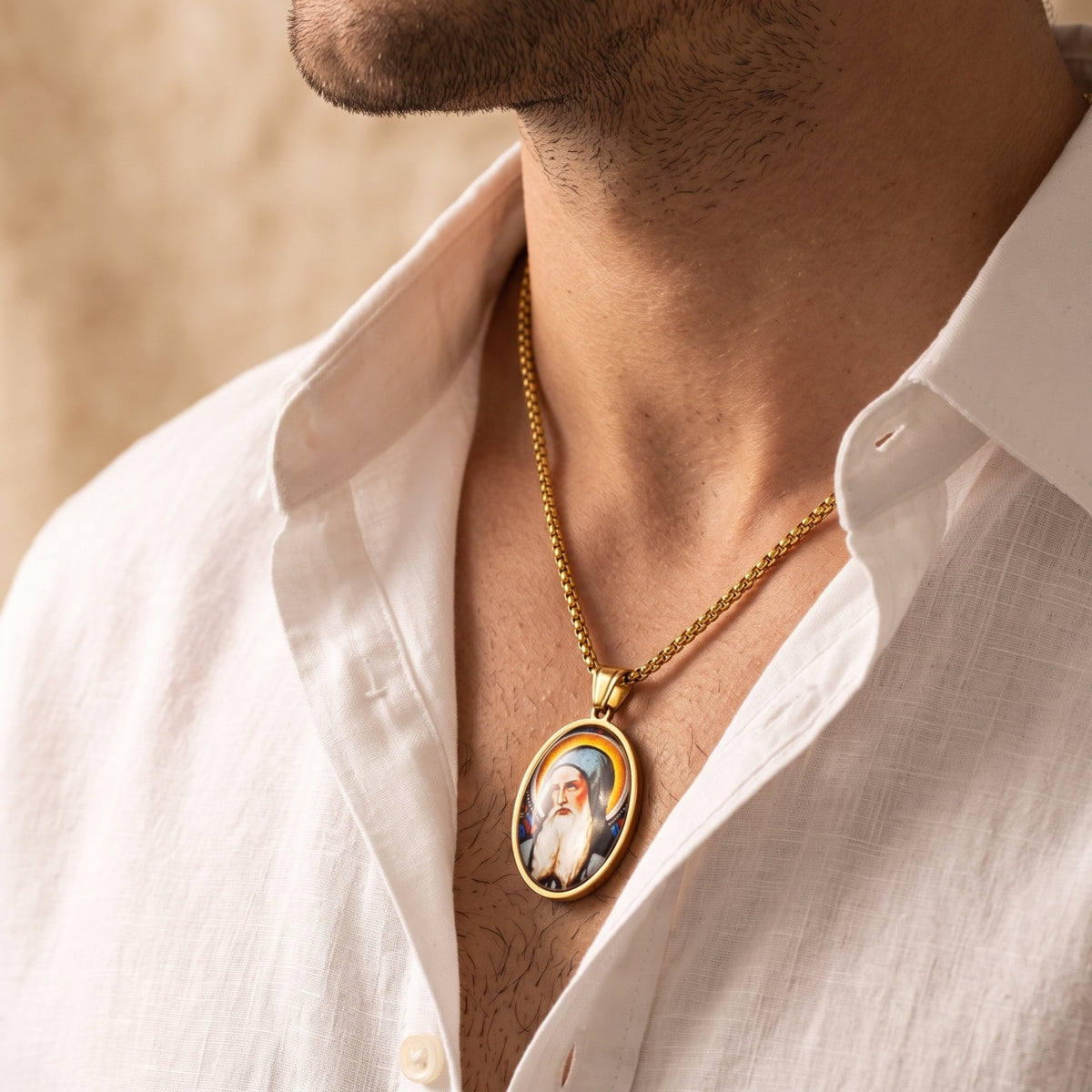 Man wearing a gold-tone oval saint pendant necklace with an open white shirt.