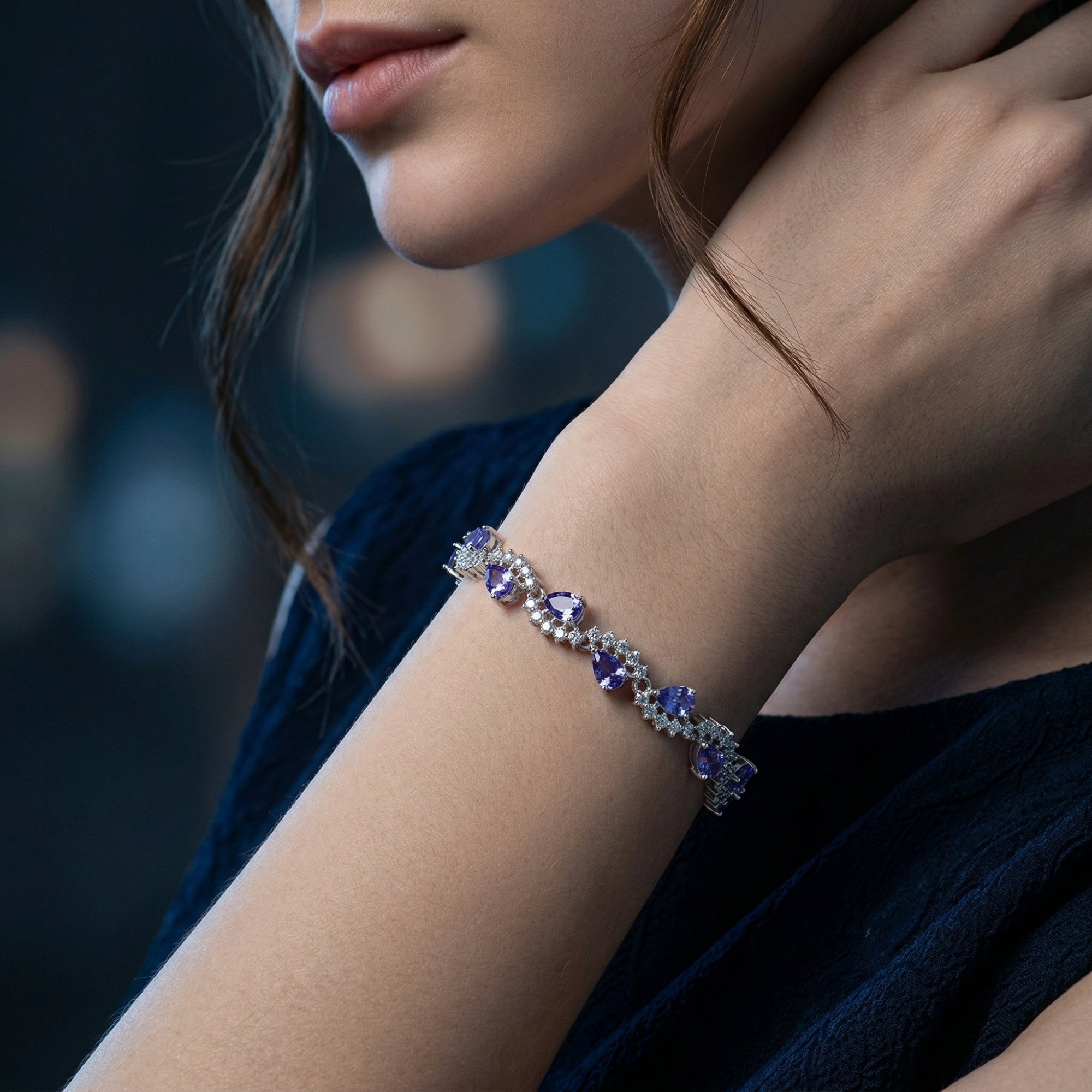 Side view of the pear cut tanzanite tennis bracelet in silver worn on a woman's wrist.