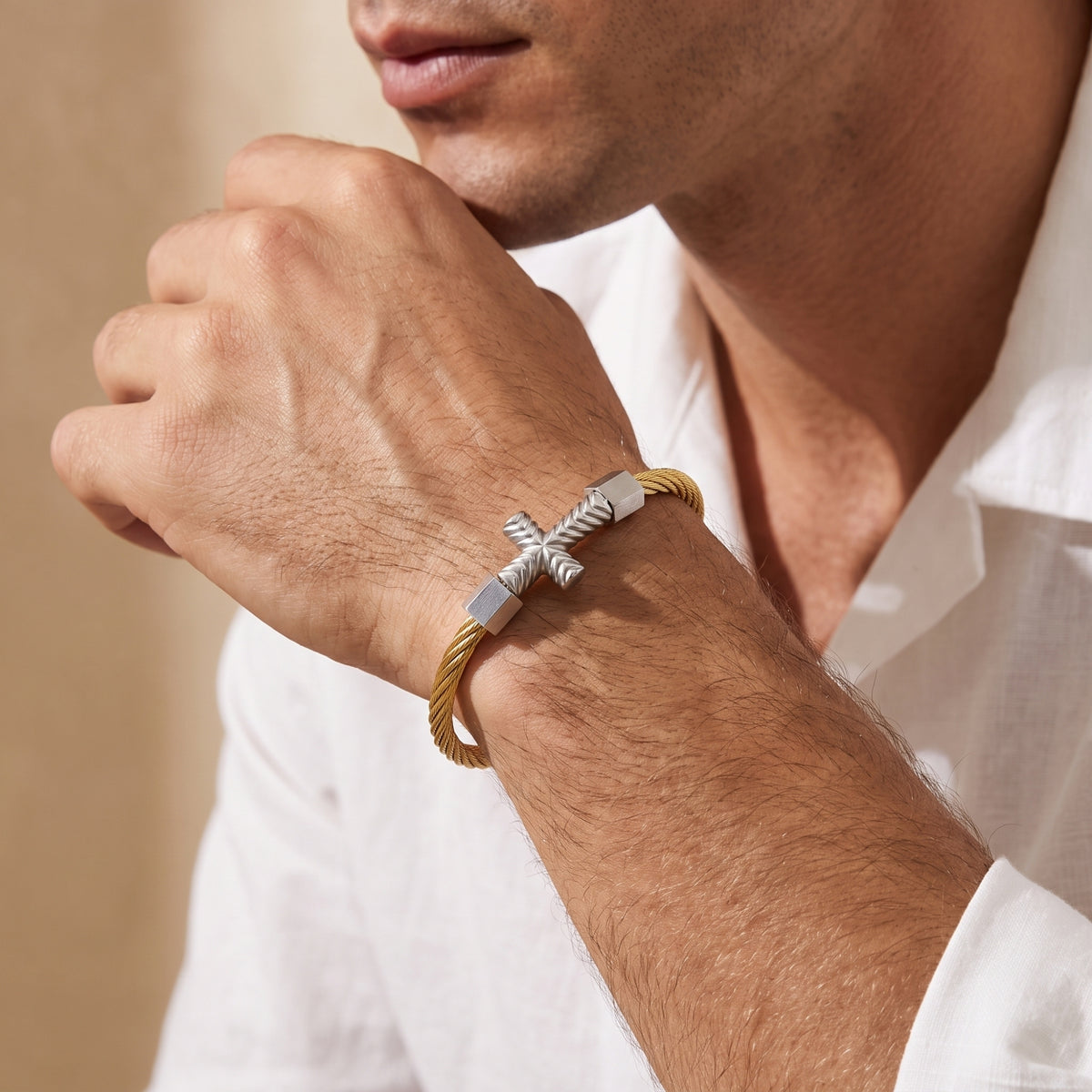 Man wearing the gold-tone cable cross bracelet while resting his hand near his chin.