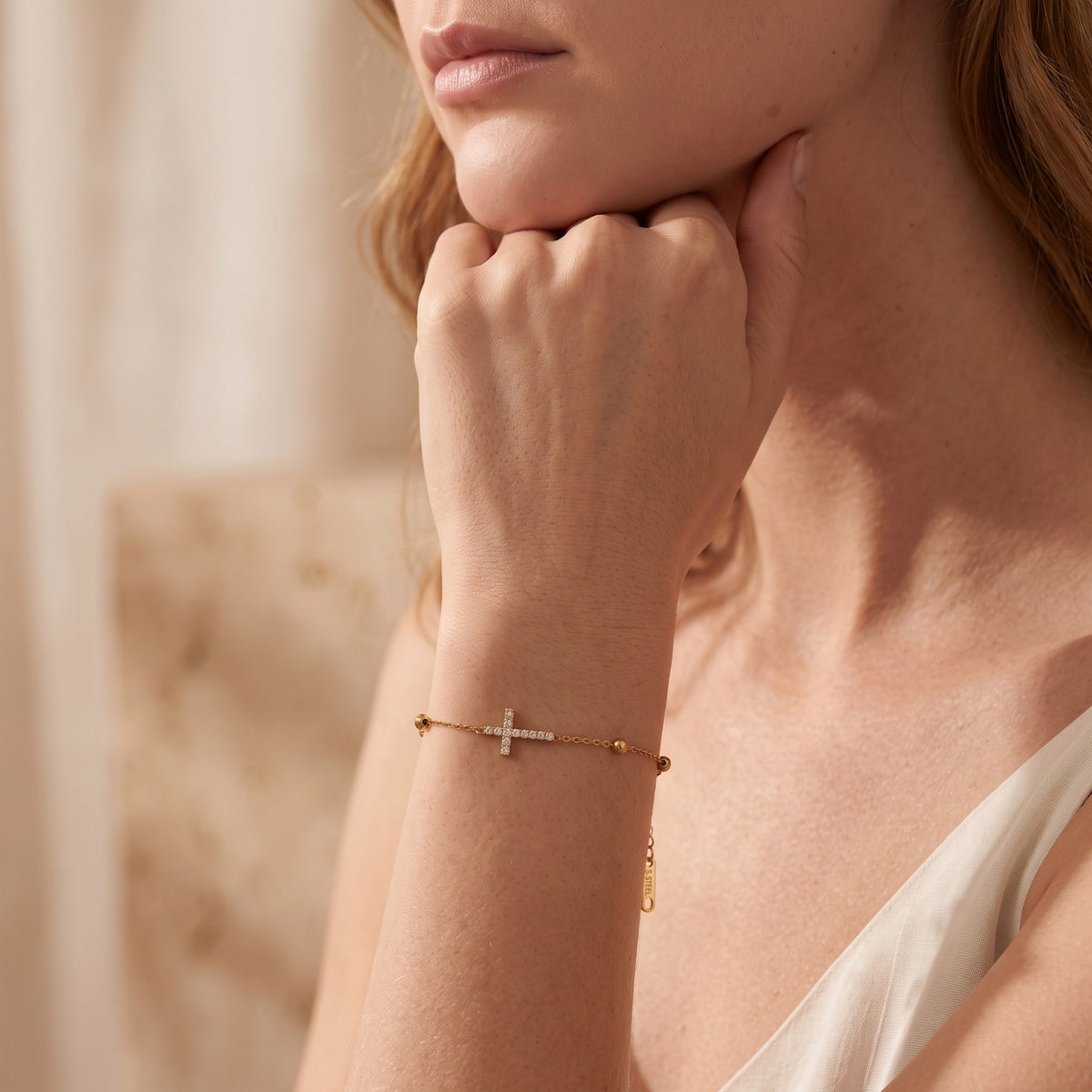 Model wearing the gold-tone pave cross bracelet on her wrist while resting her hand under her chin.