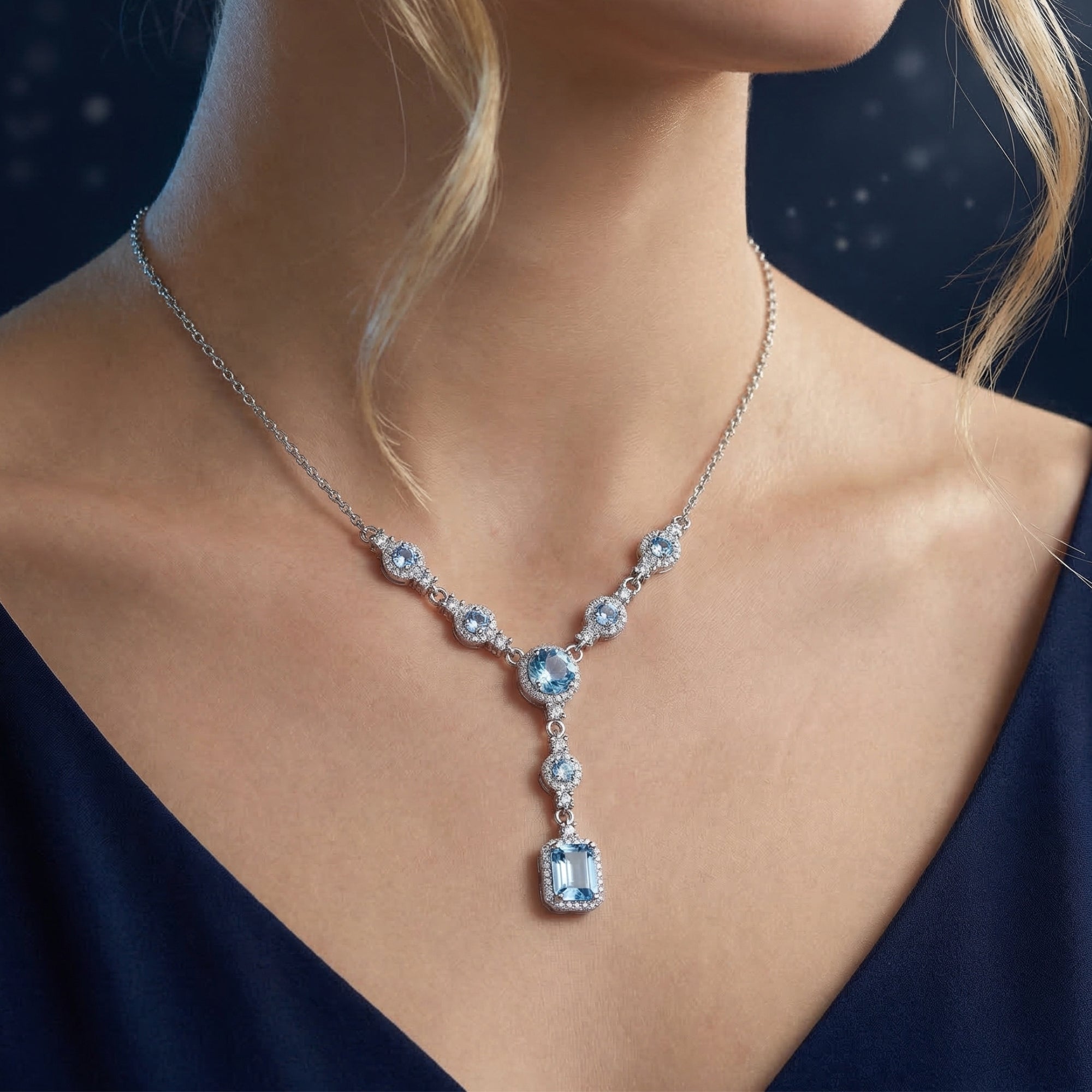 White gold cascading necklace featuring emerald and round cut blue topaz stones worn by a model.