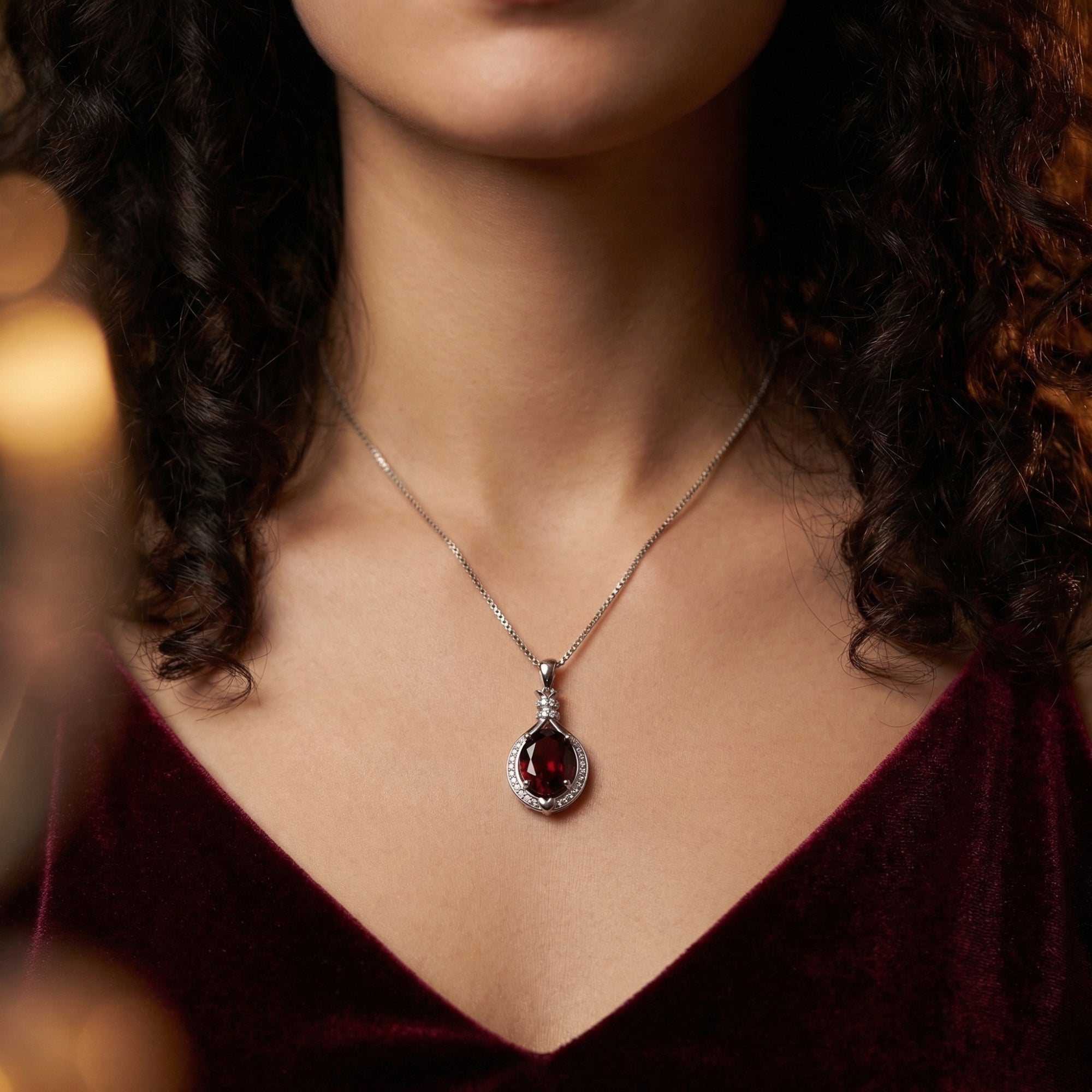 Front view of the Carmina oval garnet necklace in silver worn by a model in a dark red velvet dress.