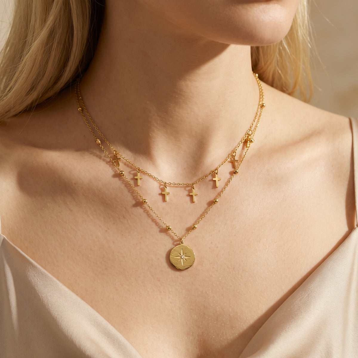 Model wearing a gold-tone layered necklace with cross charms and a star pendant over a light sleeveless top.