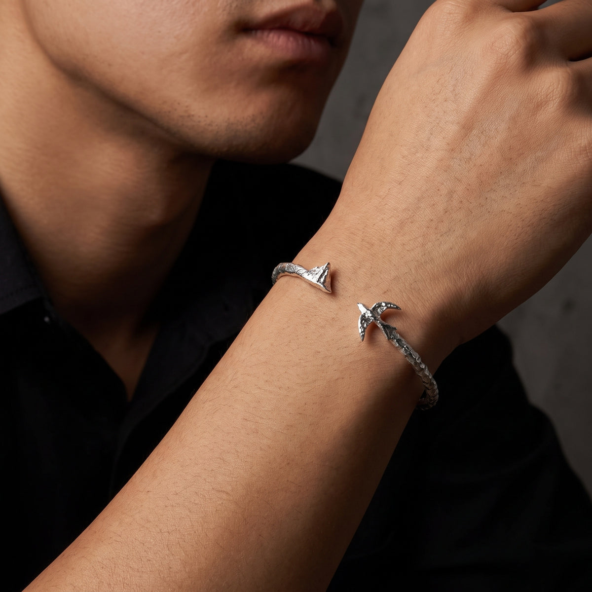 Close-up of a silver open cuff bracelet on a man's wrist, showing the gap between its mountain and bird ends.
