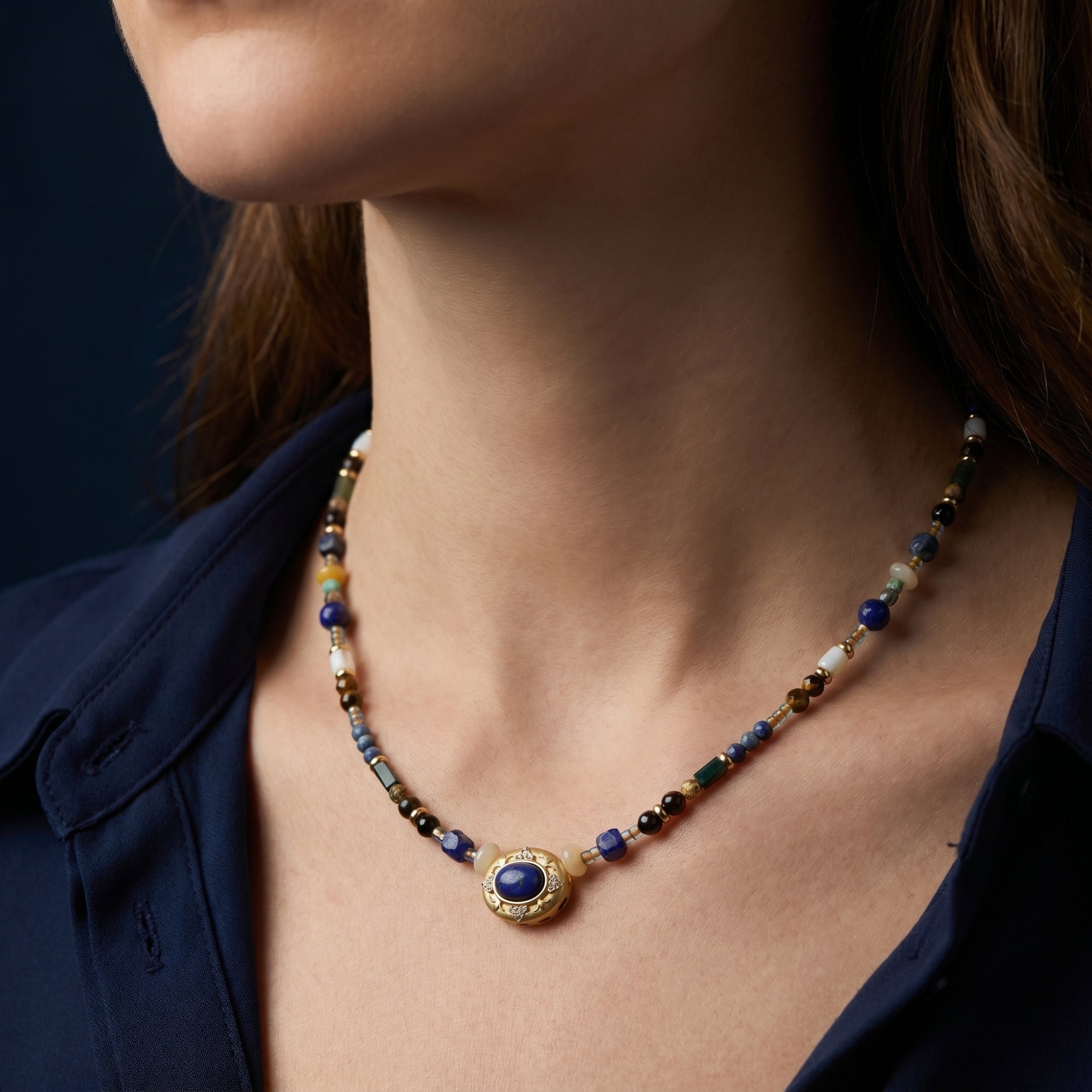 A woman wearing the gold plated lapis lazuli and tiger's eye beaded necklace against a dark background.