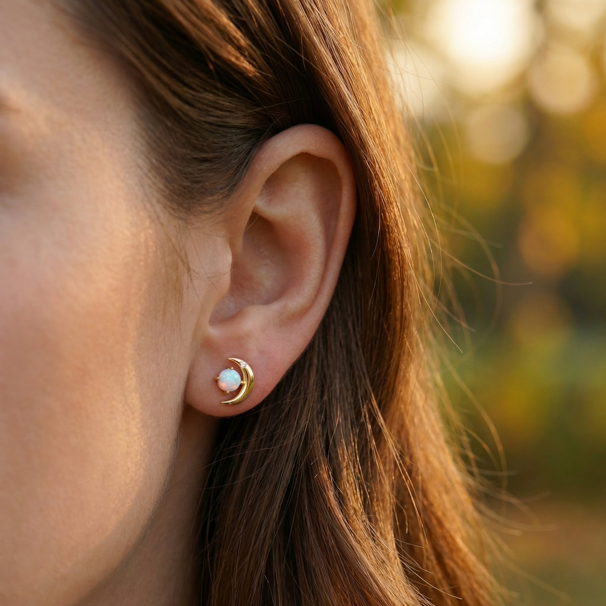 Profile view of a model wearing a gold-tone crescent moon stud earring featuring a round natural opal stone.