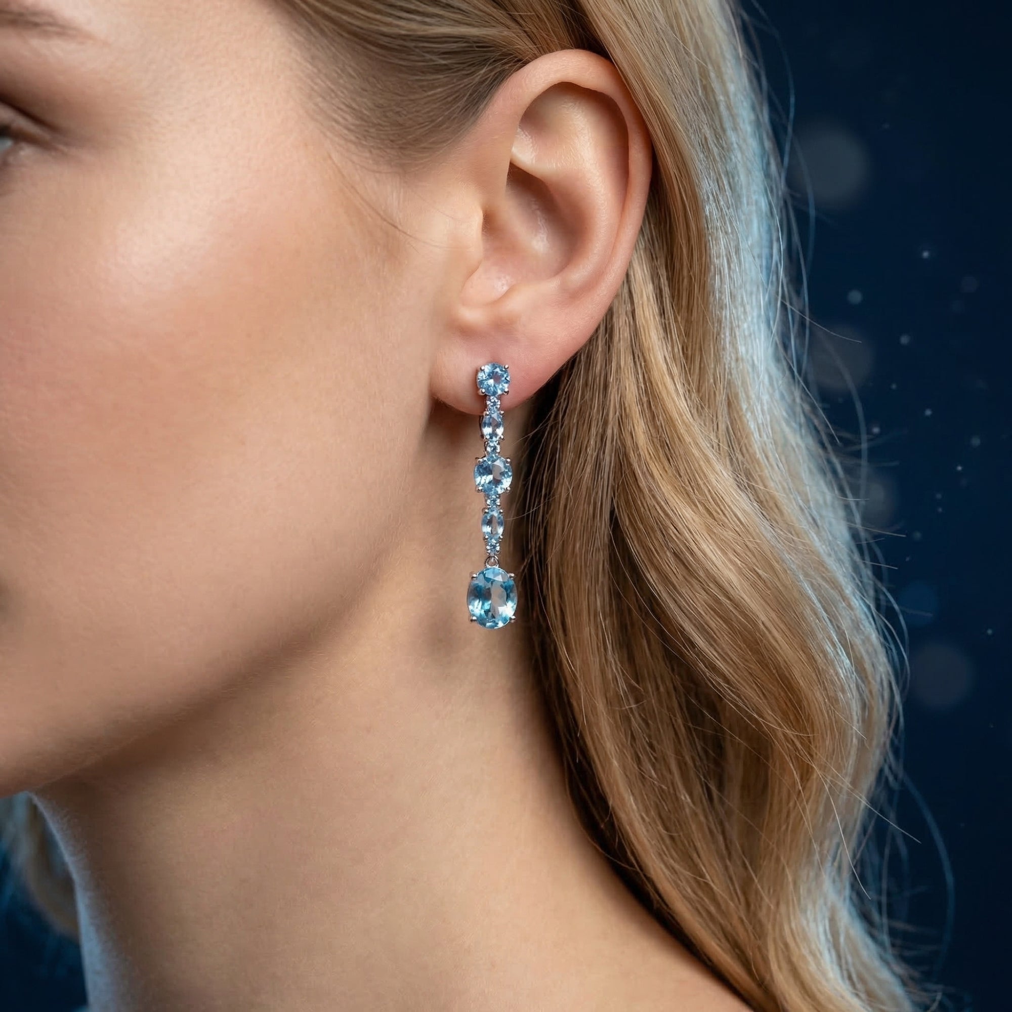 Model wearing a silver cascade earring featuring vibrant natural blue round and oval cut topaz stones.