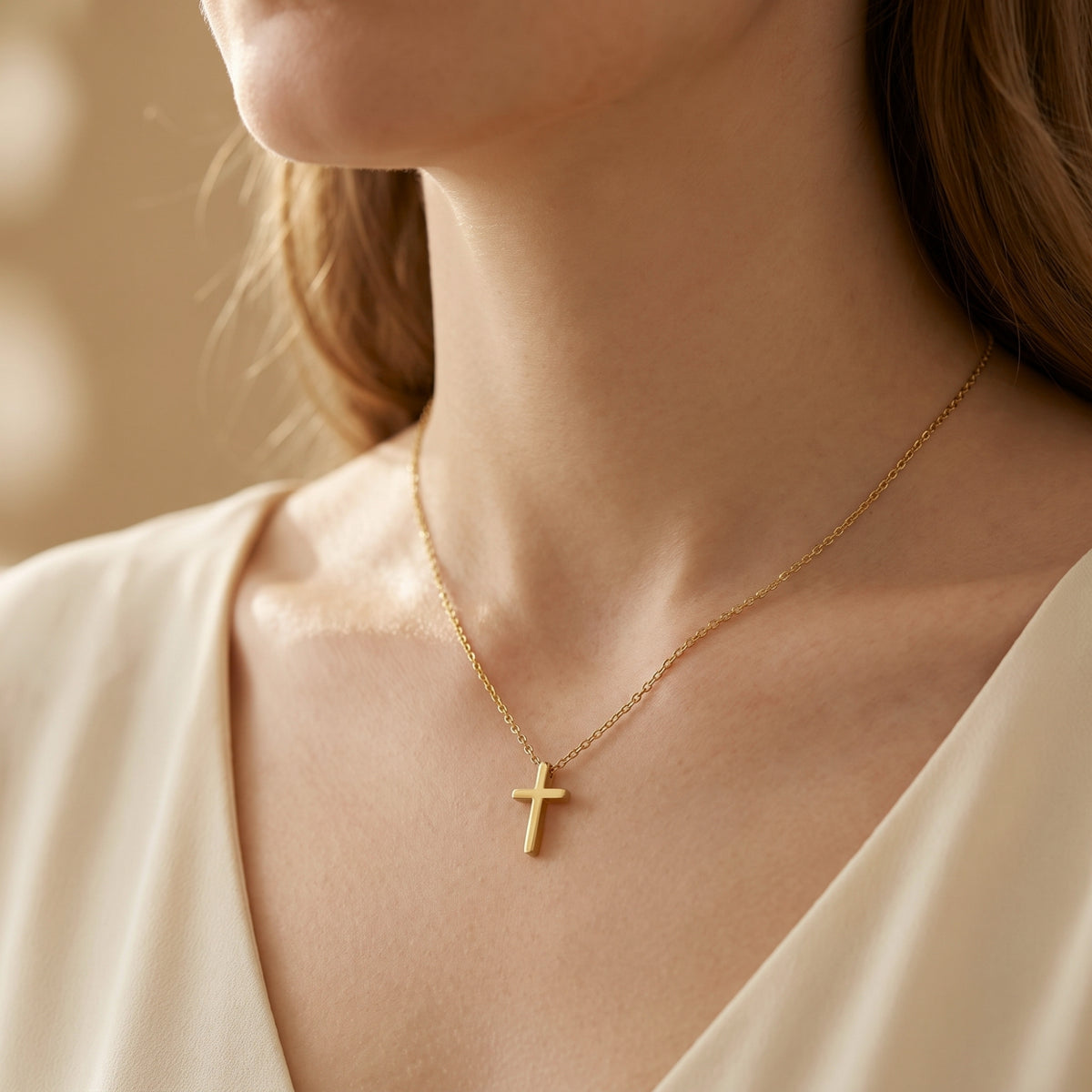 Close-up front view of a woman wearing a polished gold-tone cross necklace over a cream top.