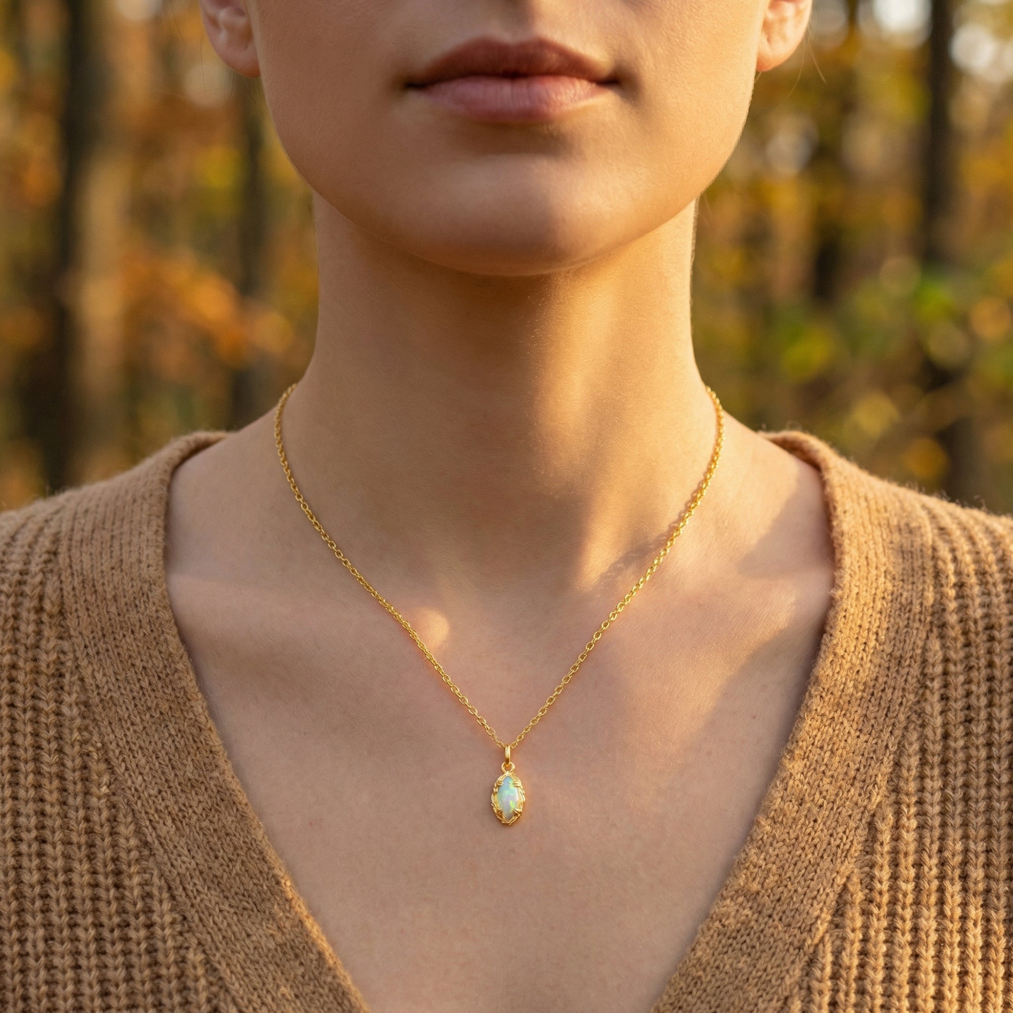 Front view of a model wearing the gold marquise-cut white opal necklace against a blurred forest background.