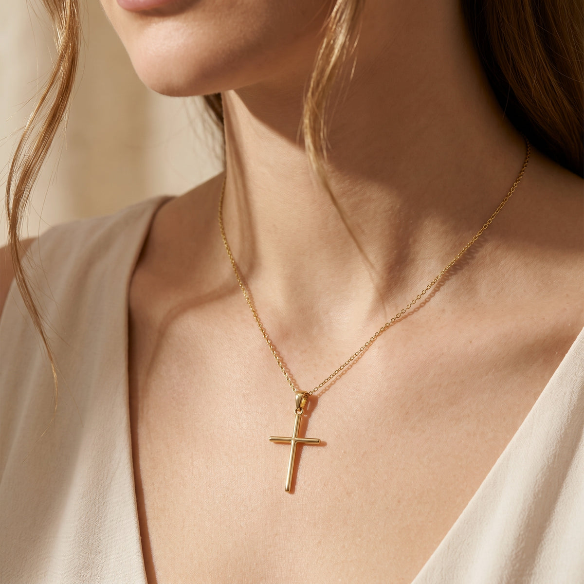 A gold-tone cross necklace displayed around the neck of a model wearing a sleeveless neutral top.