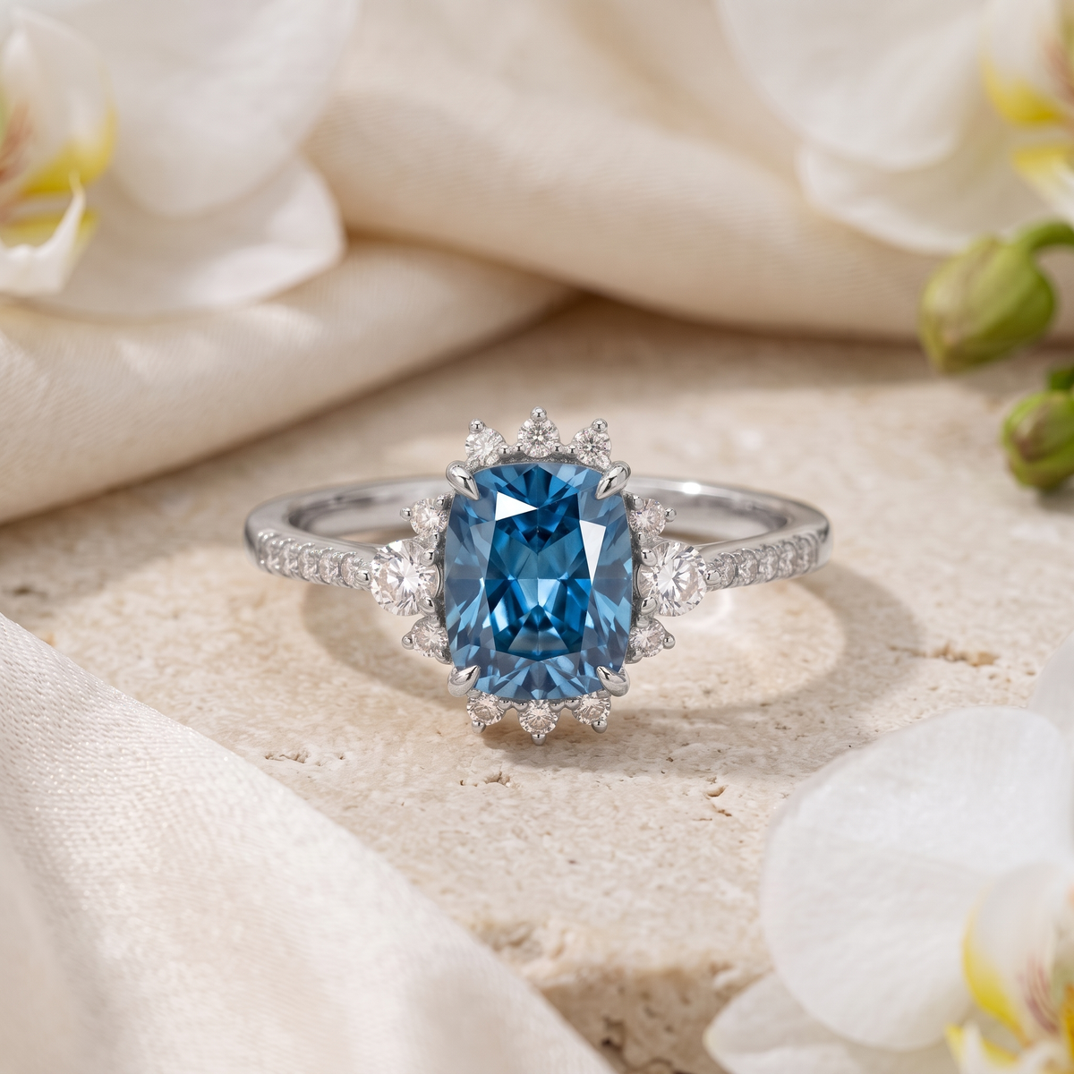 A white gold cushion-cut blue moissanite engagement ring with a diamond halo on a beige stone surface.