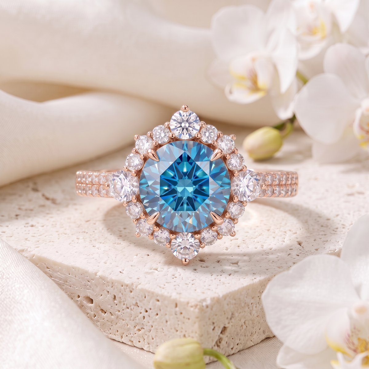 Rose gold halo engagement ring featuring a round blue moissanite center stone resting on stone with white orchids.