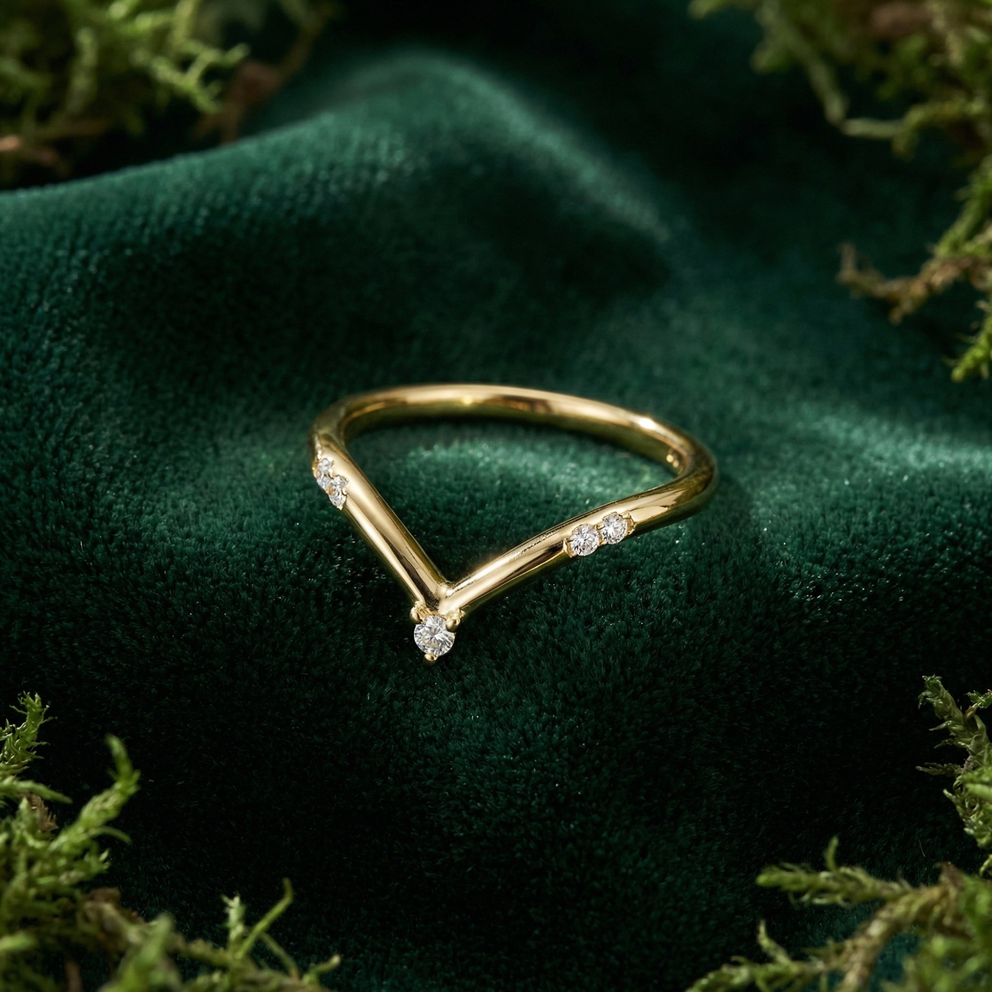 Gold-plated chevron band with small clear stones on a green velvet surface.