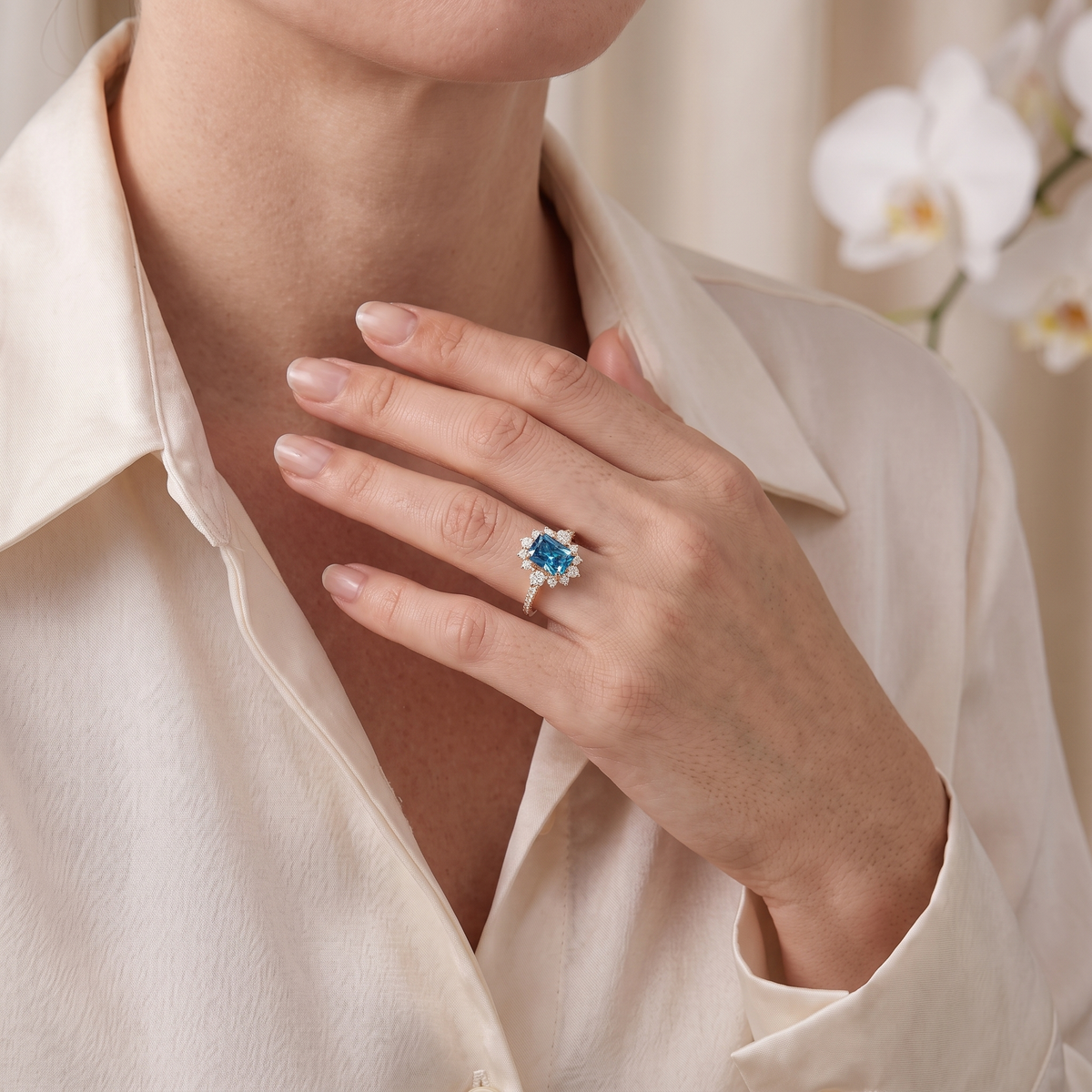 Model wearing the rose gold radiant-cut blue moissanite halo engagement ring against a silk blouse.
