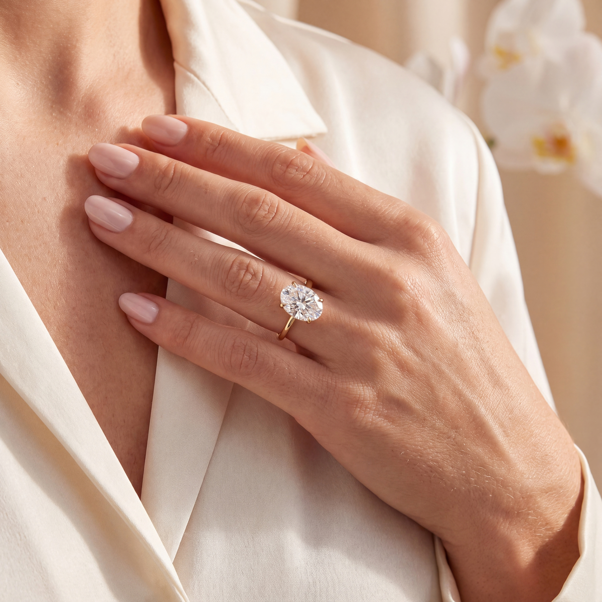 Model resting her hand near her collarbone wearing the yellow gold oval moissanite solitaire engagement ring.