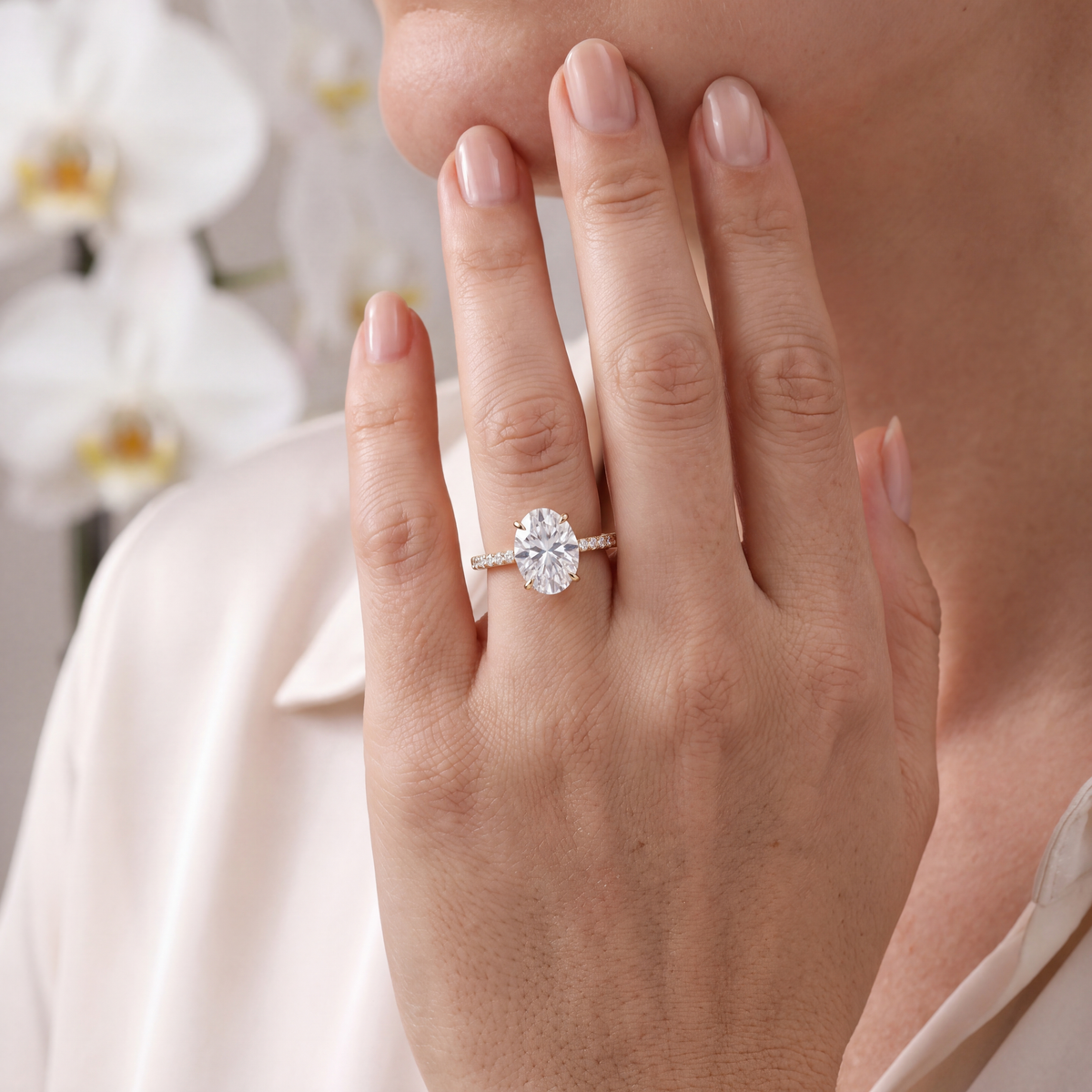 A woman wearing a gold oval moissanite engagement ring, resting her hand near her chin.
