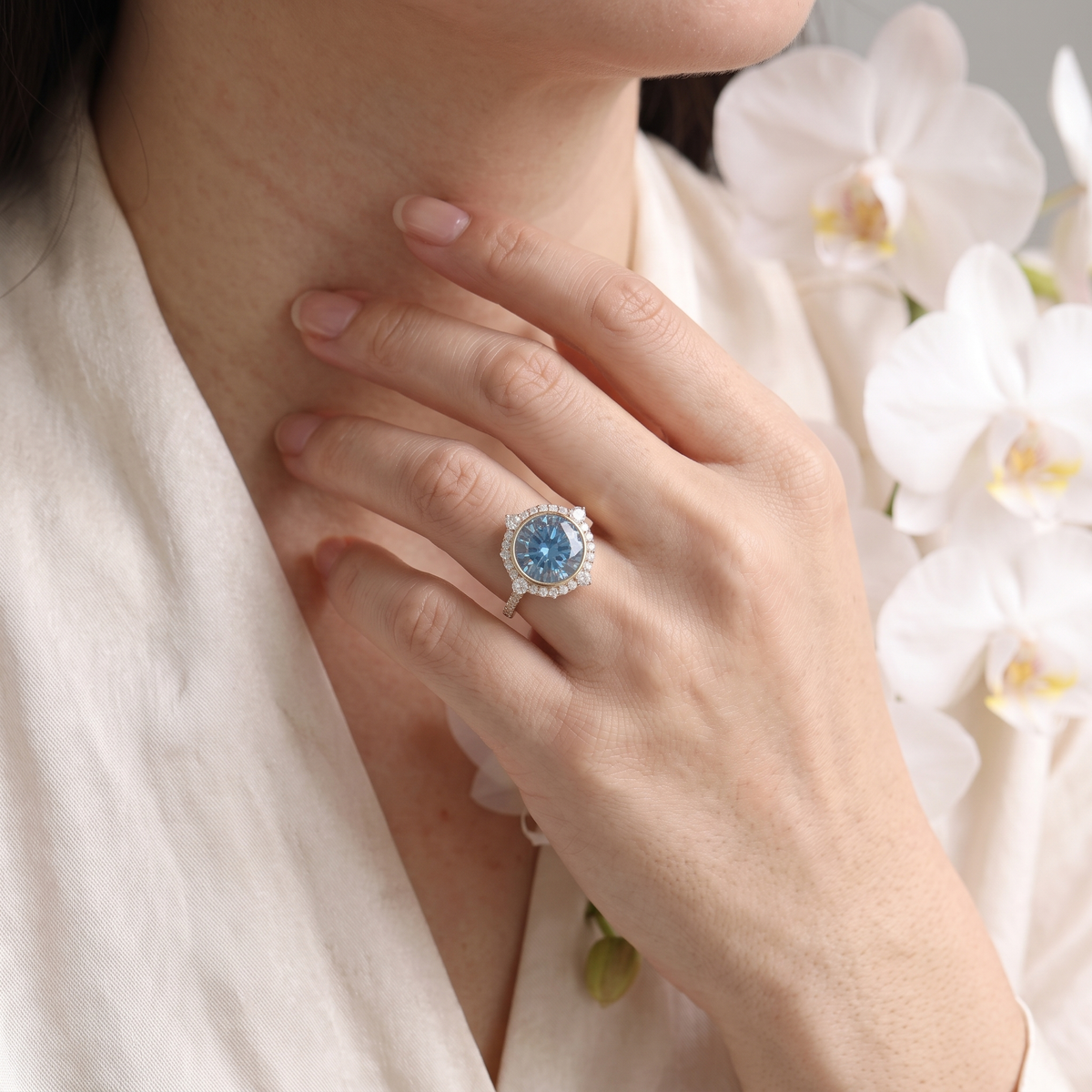 Close-up of a model wearing a round blue moissanite halo engagement ring in rose gold.