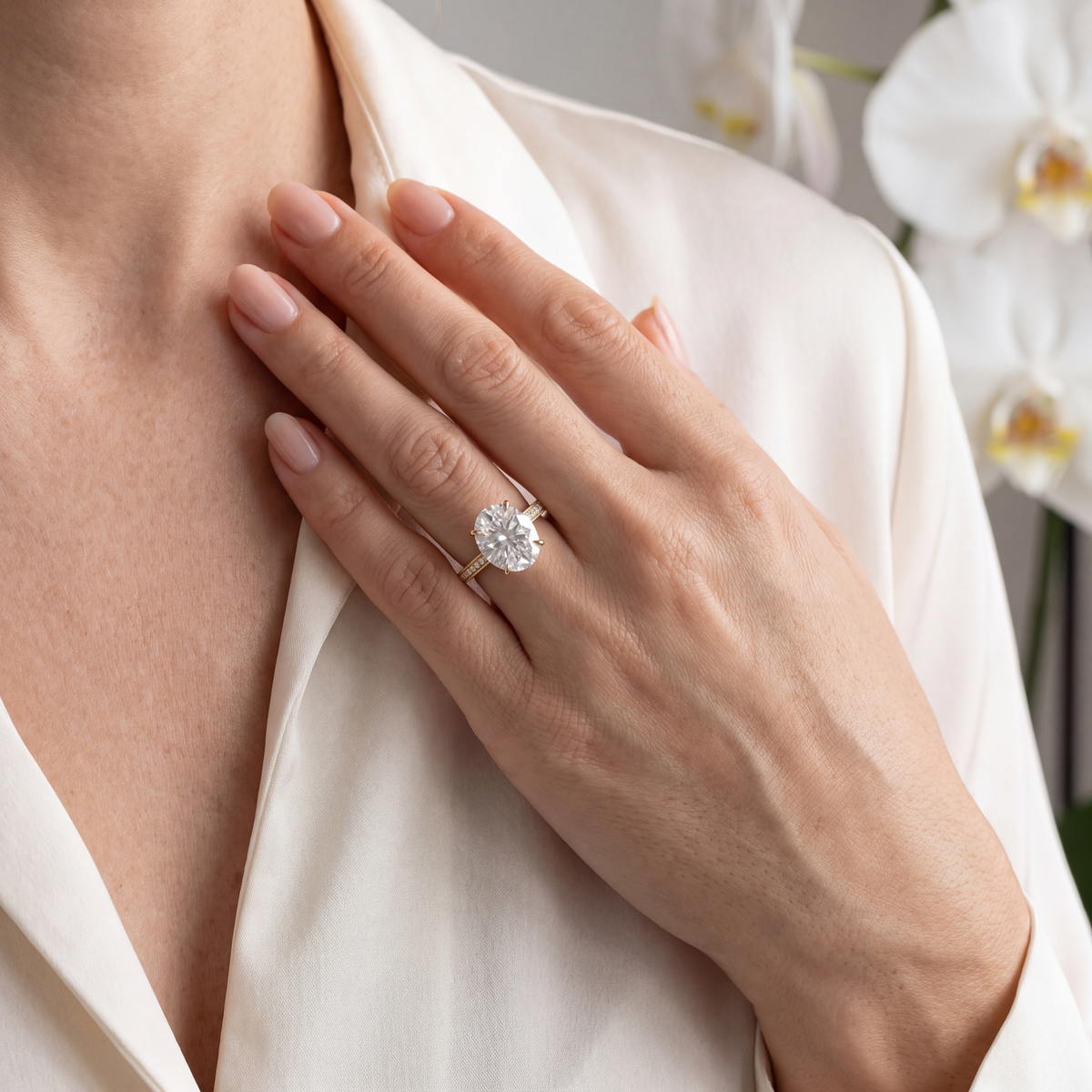 Yellow gold oval moissanite engagement ring worn on hand paired with a silk blouse.