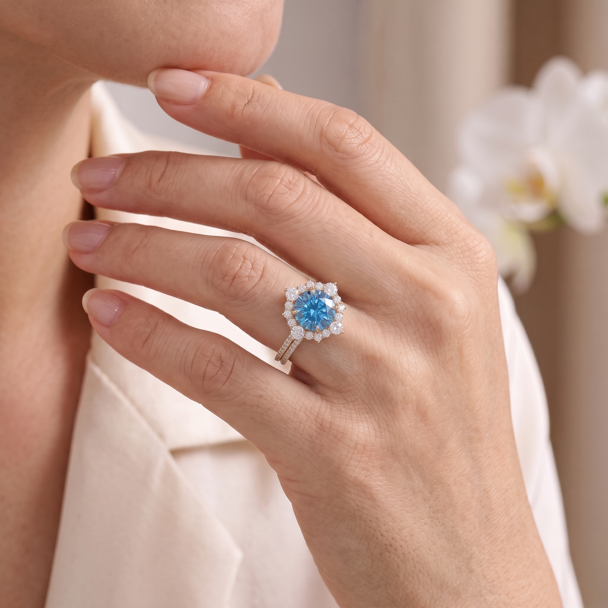Close-up of a model wearing a rose gold blue moissanite halo ring against her face and silk blouse.