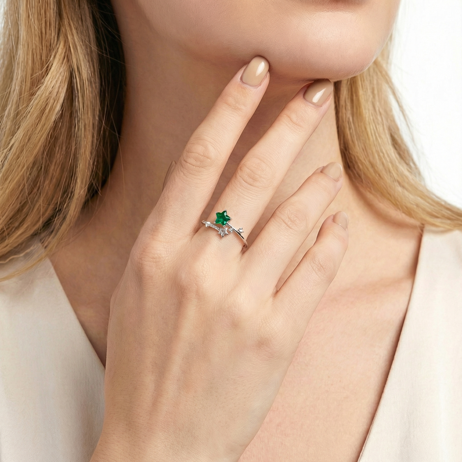Close-up of a woman's hand wearing the adjustable silver star ring with green simulated emerald stones.