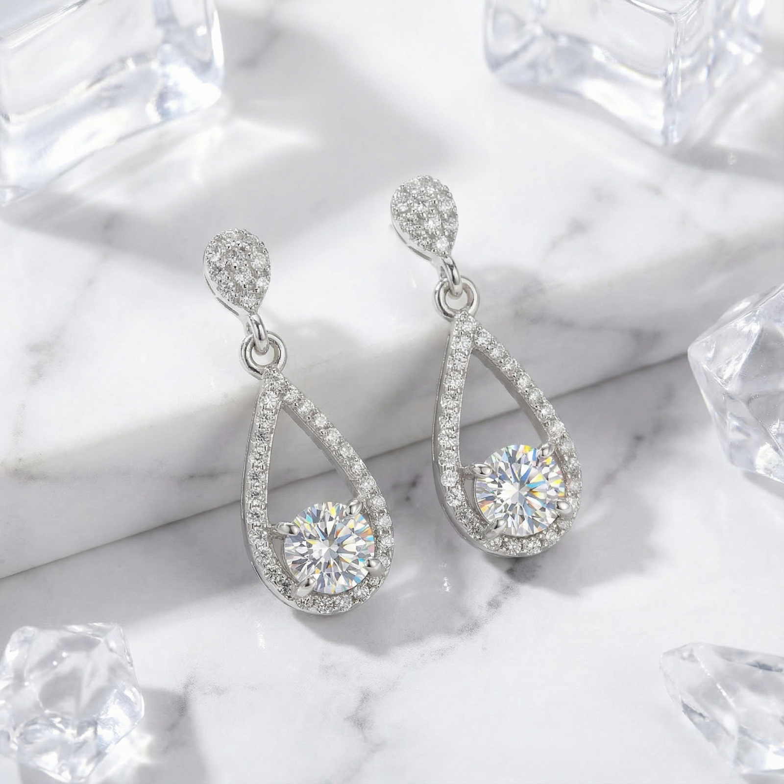 Teardrop sterling silver drop earrings with round zirconia stones on a marble surface with ice cubes.