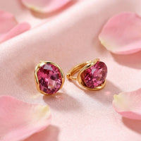 Oval pink tourmaline earrings in 18K gold plated settings on pink silk fabric with rose petals.