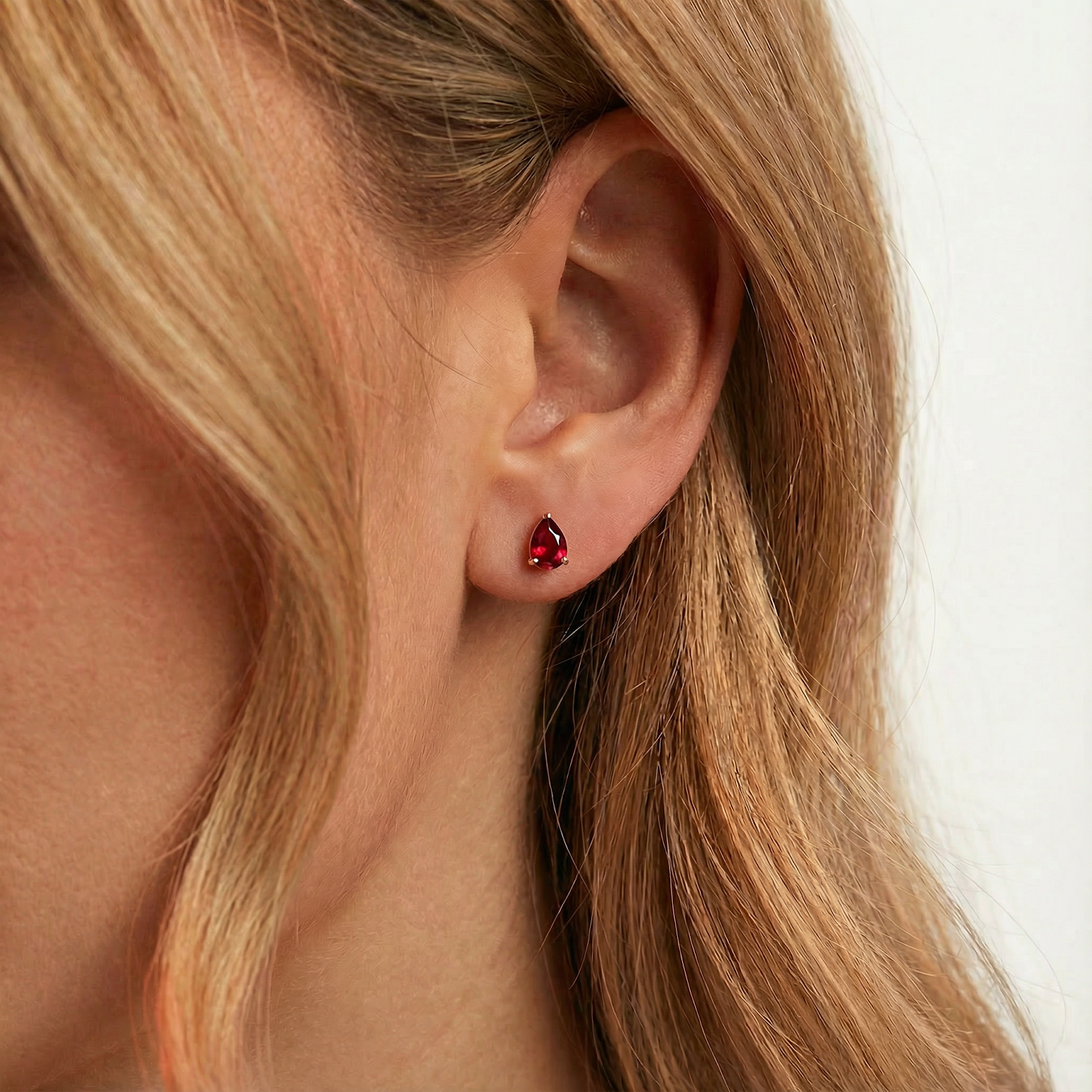 Close-up of a pear-shaped simulated ruby stud earring in 18K gold vermeil worn on an ear.