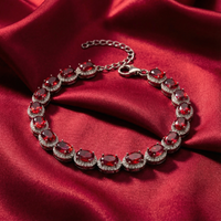 Oval-cut simulated ruby tennis bracelet in sterling silver displayed on red satin fabric.