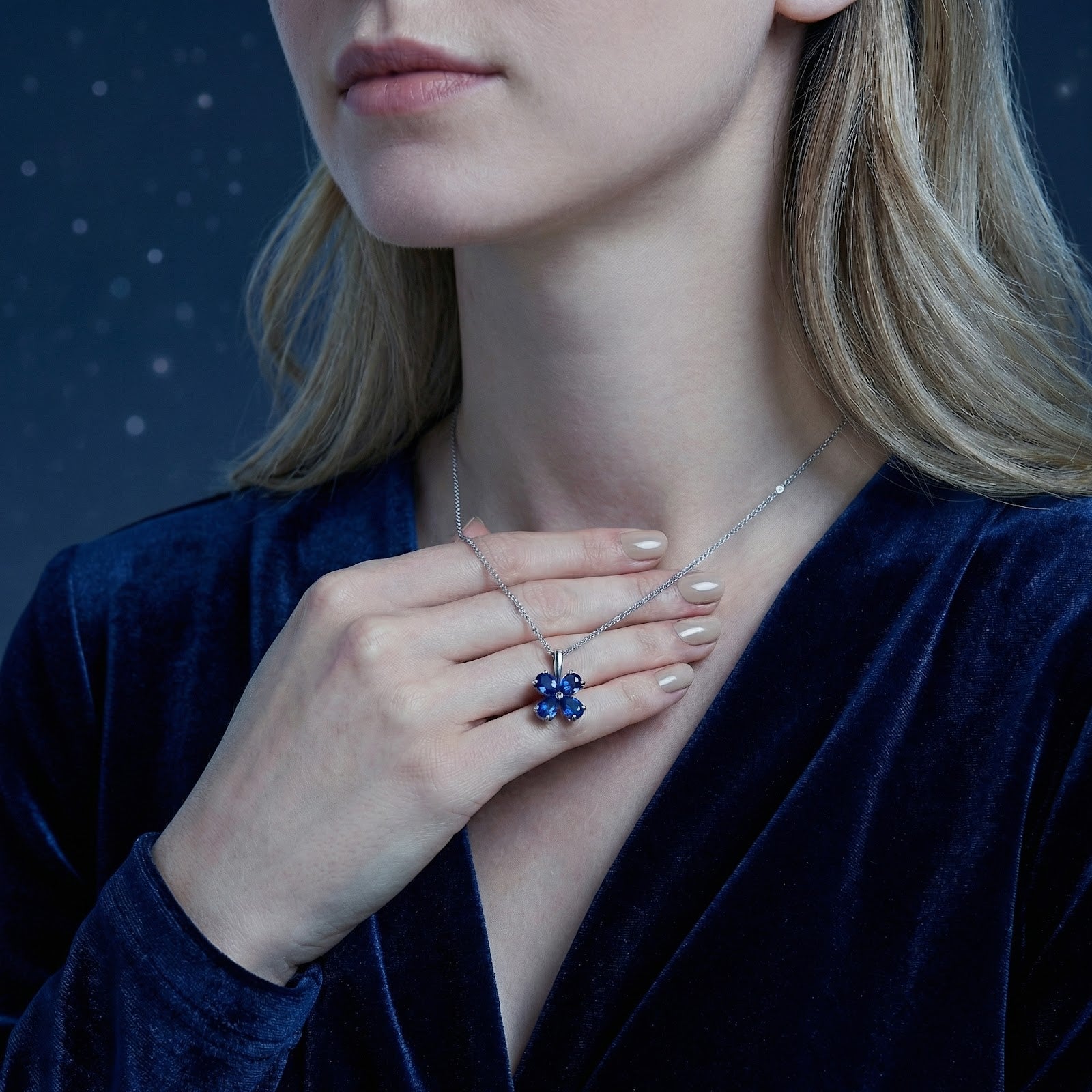 Sterling silver heart-cut simulated sapphire clover necklace held by a model to show product scale.