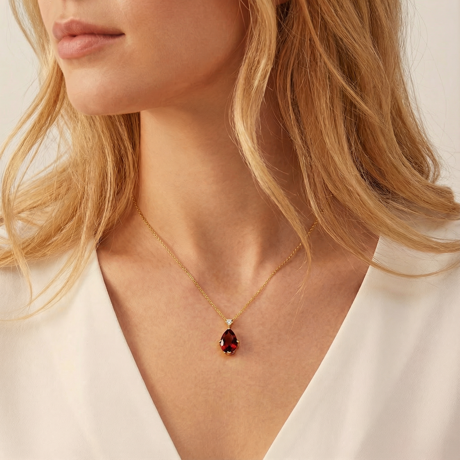 A woman wearing the 18K gold vermeil Adalene Teardrop necklace featuring a pear cut simulated garnet.