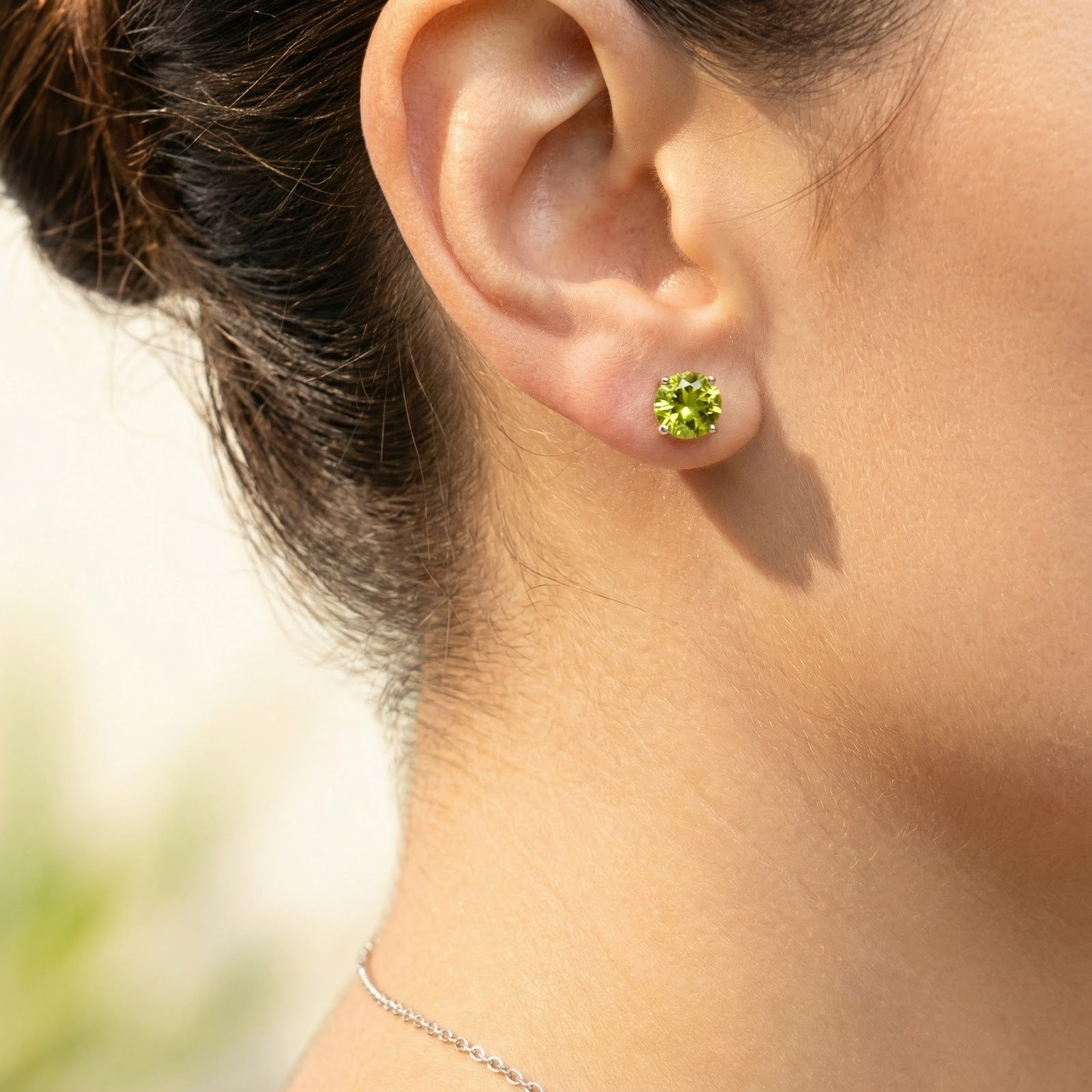 Woman wearing a round-cut simulated peridot stud earring in a sterling silver setting on her earlobe.