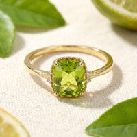 Cushion cut simulated peridot ring in 18K gold vermeil on a textured surface with citrus leaves.