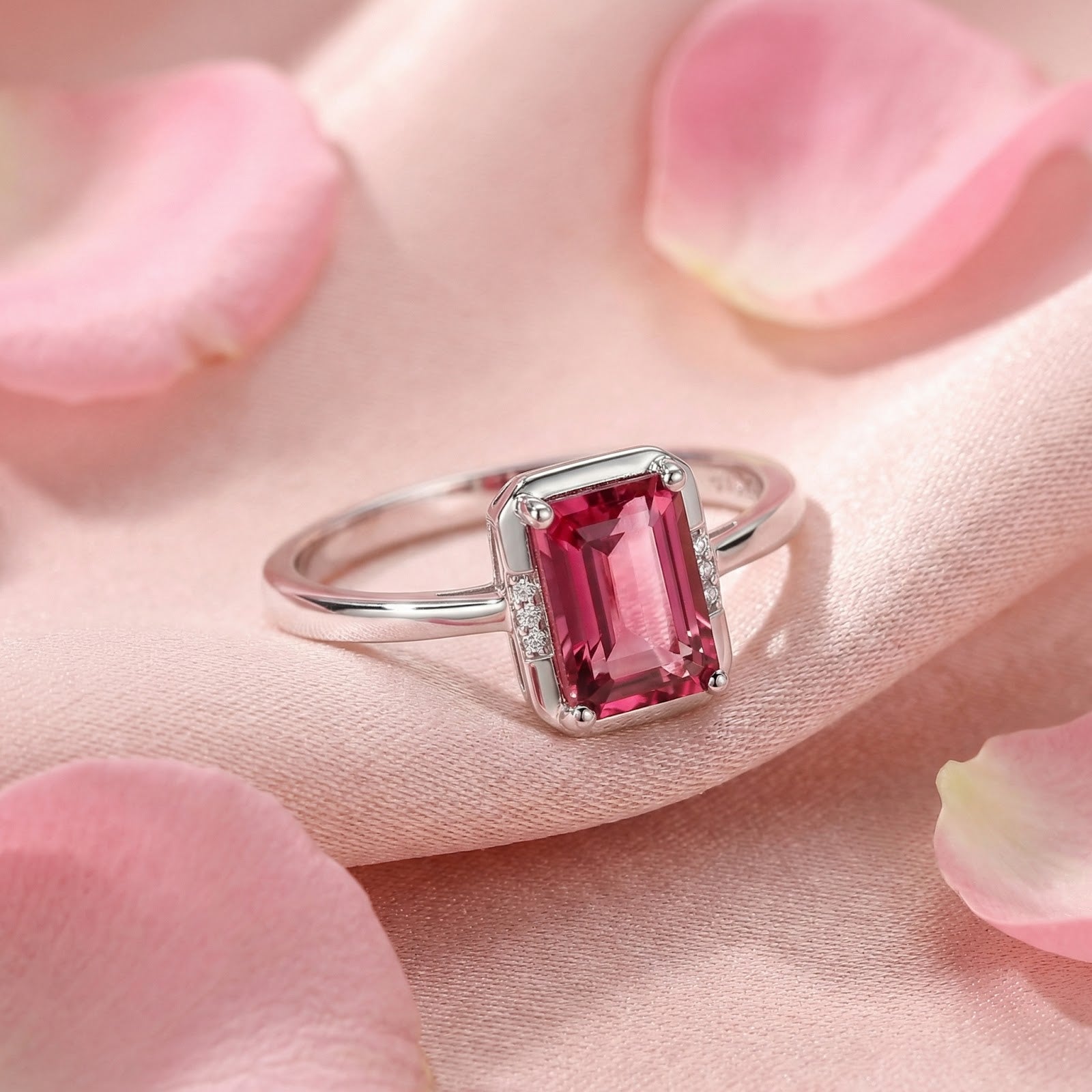 Emerald-cut pink tourmaline ring in sterling silver resting on pink silk fabric with rose petals.