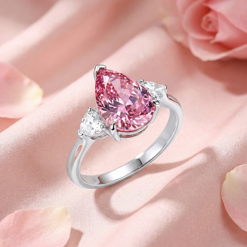 Angled view of a pear-cut simulated pink tourmaline S925 sterling silver ring resting on pink fabric with petals.