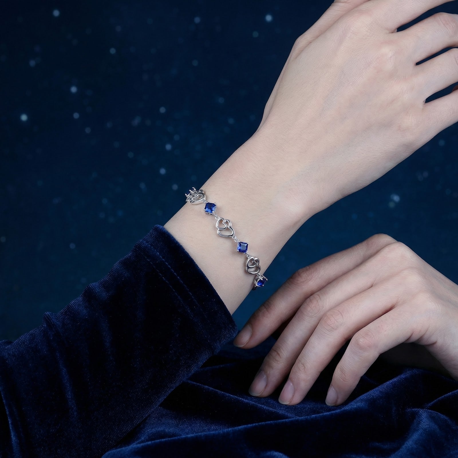 S925 sterling silver heart-link bracelet with blue simulated sapphires worn on a woman's wrist against a starry sky.