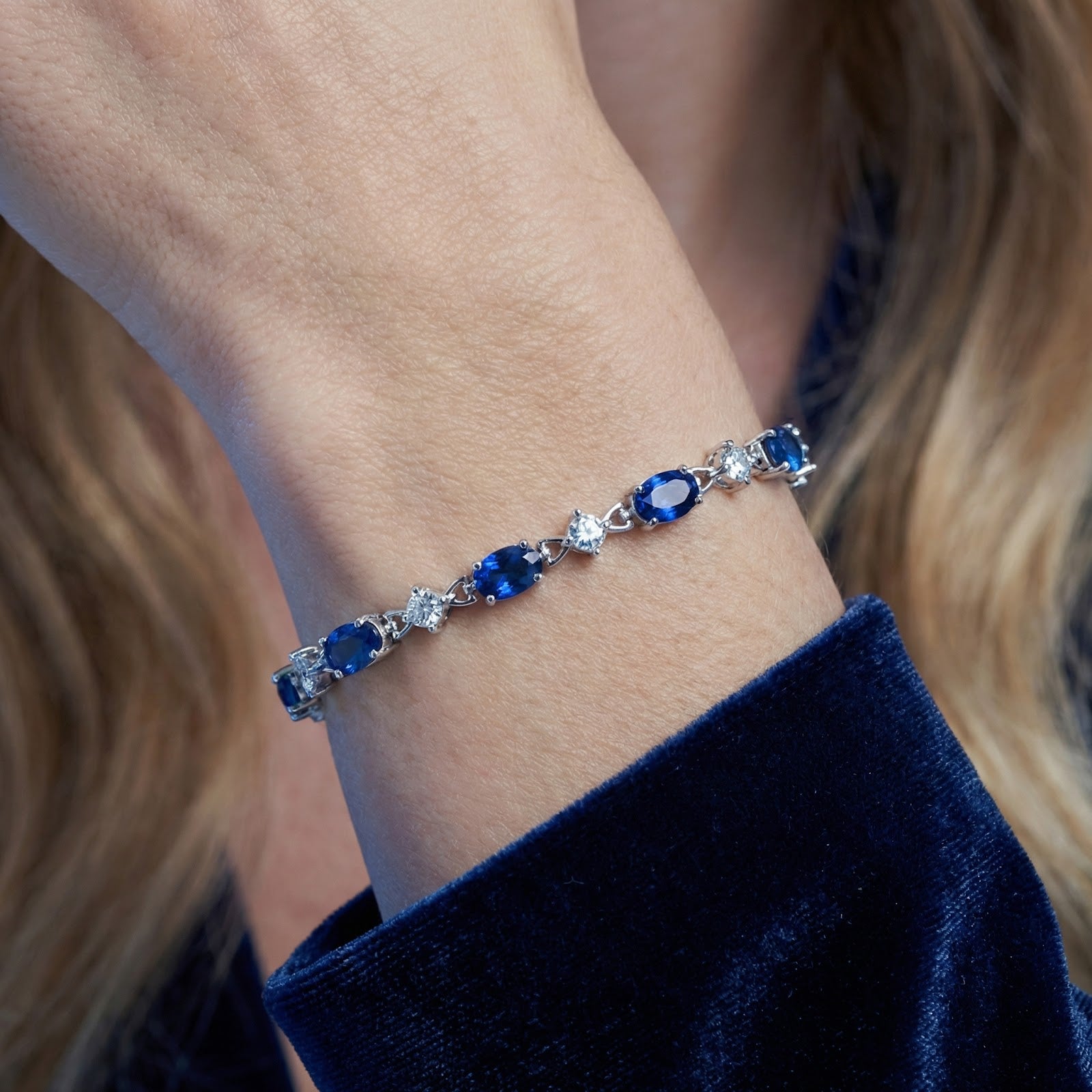 Macro shot of oval-cut blue simulated sapphires and silver settings on the Neriselle bracelet worn on a wrist.