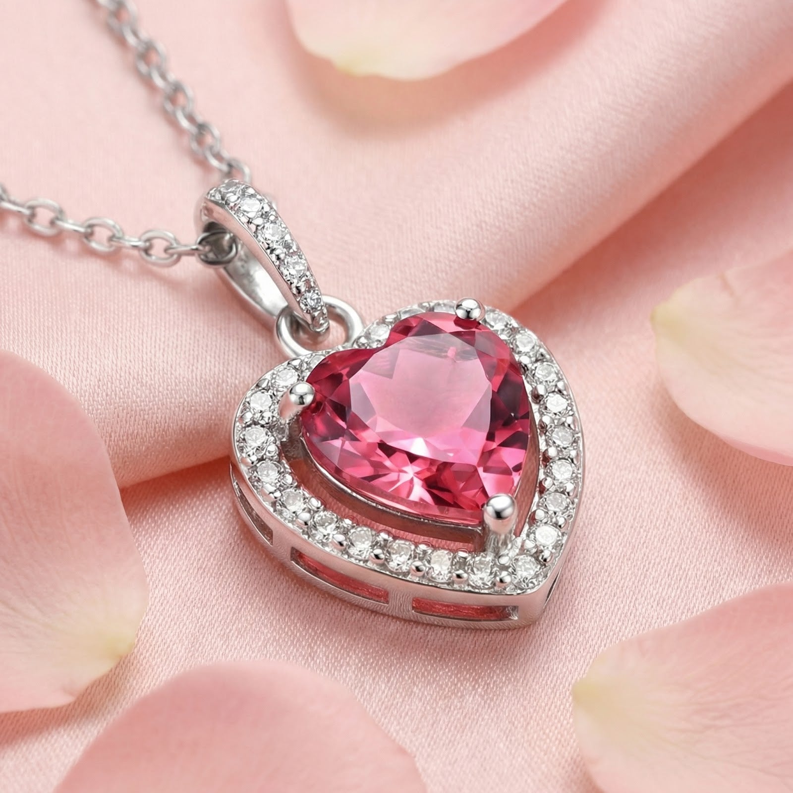 Heart-cut pink tourmaline necklace in sterling silver with a halo setting, resting on pink silk and rose petals.