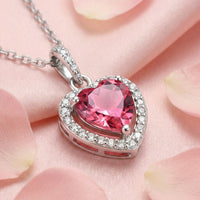 Heart-cut pink tourmaline necklace in sterling silver with a halo setting, resting on pink silk and rose petals.